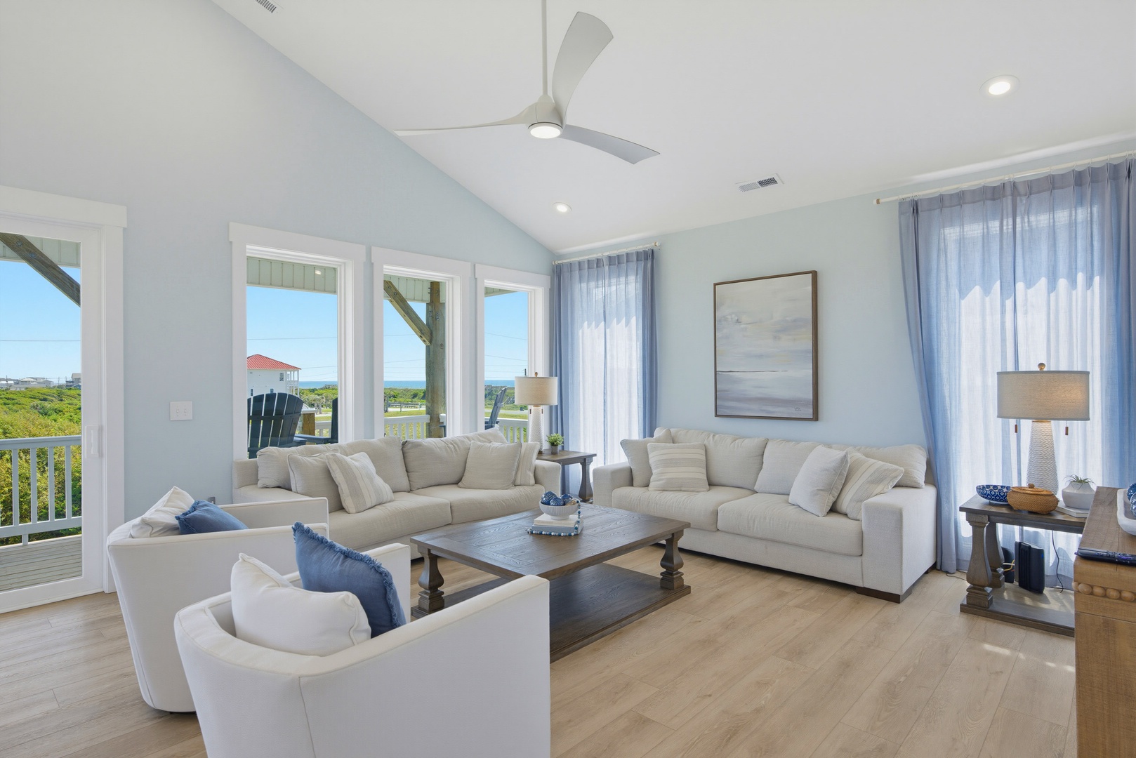 Relax in this bright, airy living room with soaring ceilings and views of coastal greenery. Sink into plush seating, feel the breeze from the ceiling fan, and enjoy the natural light streaming through the windows.
