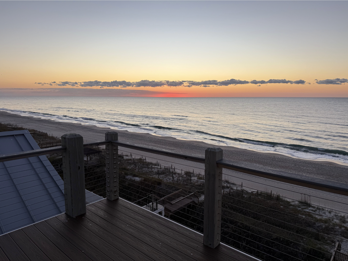 A tranquil oceanfront setting where soft dawn light brushes the horizon, gentle waves meet sandy shore, and the nearby terrace offers a peaceful vantage point to start your day.