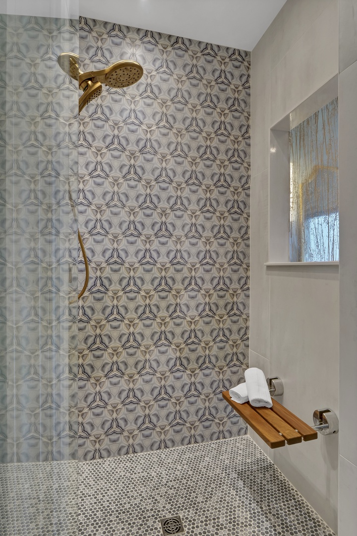 Refresh under your elegant rain shower, surrounded by beautiful patterned tile and thoughtful touches like a teak bench for comfort.