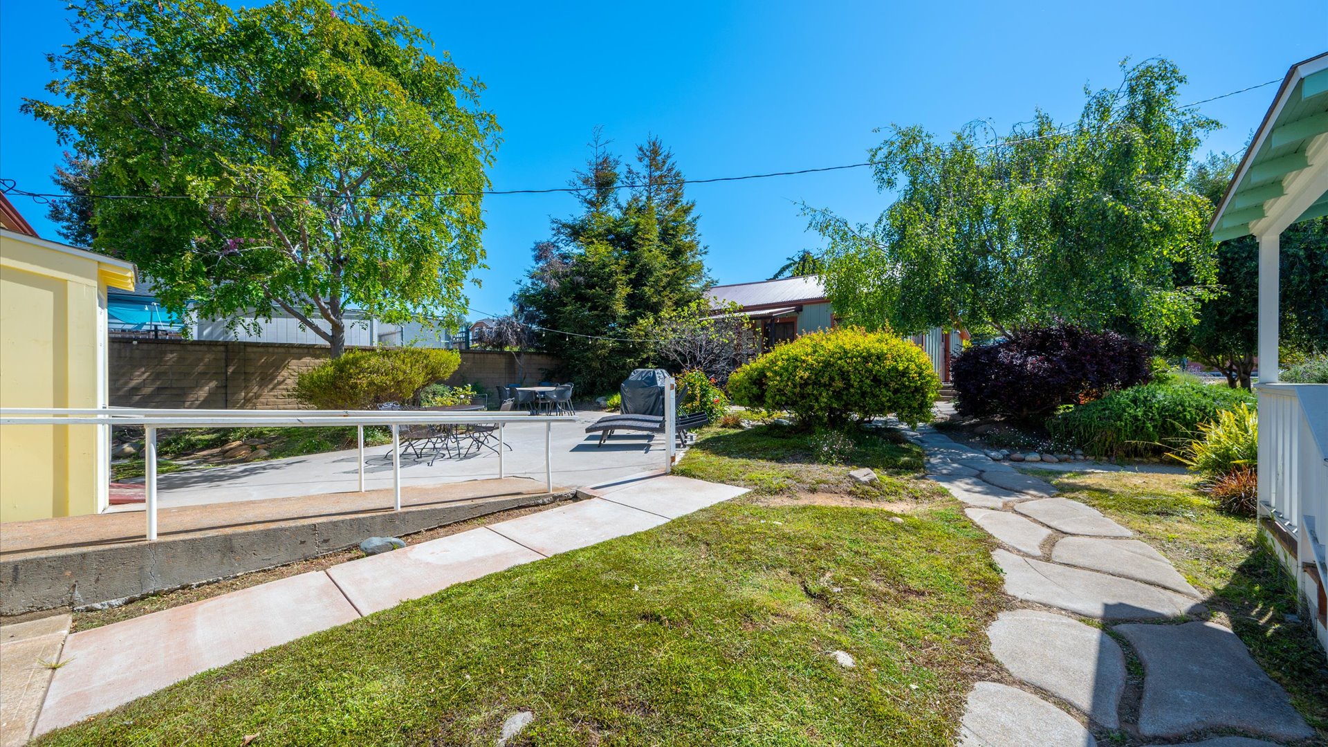 Enjoy sunny days in this beautifully landscaped yard with lush greenery, winding stone pathways, and peaceful seating areas perfect for relaxing outdoors under blue skies.