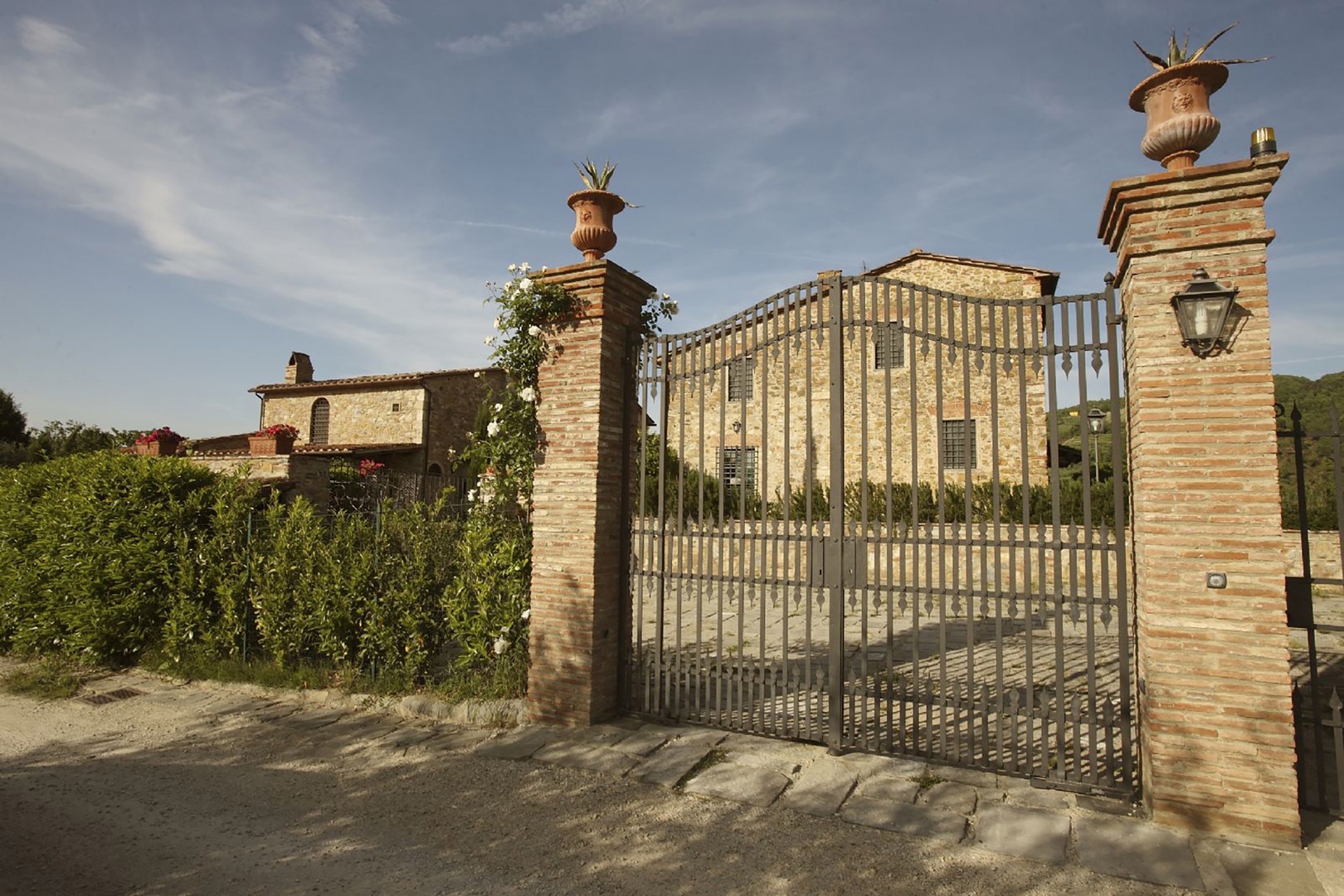 The front gate leads to a generous, paved parking area outside the villa.