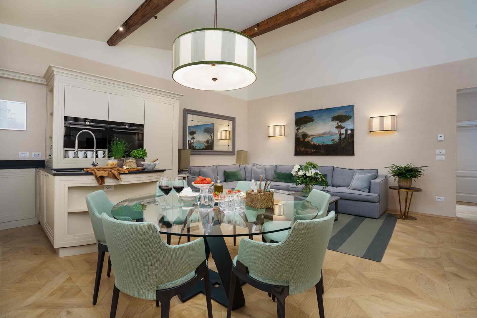 Open-concept retreat with rustic wooden beams, glass dining table, and plush gray sectional.