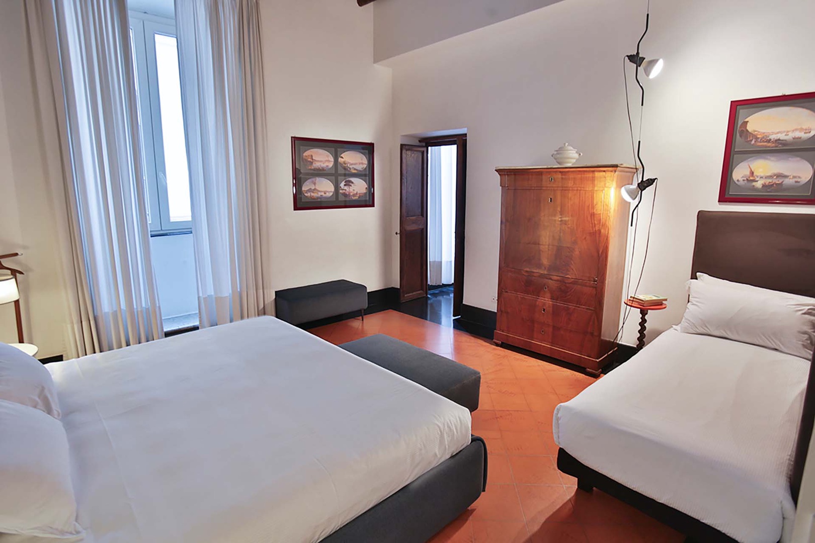 Your spacious bedroom features twin beds with crisp linens, classic wooden furniture, and warm terracotta floors creating a comfortable retreat.