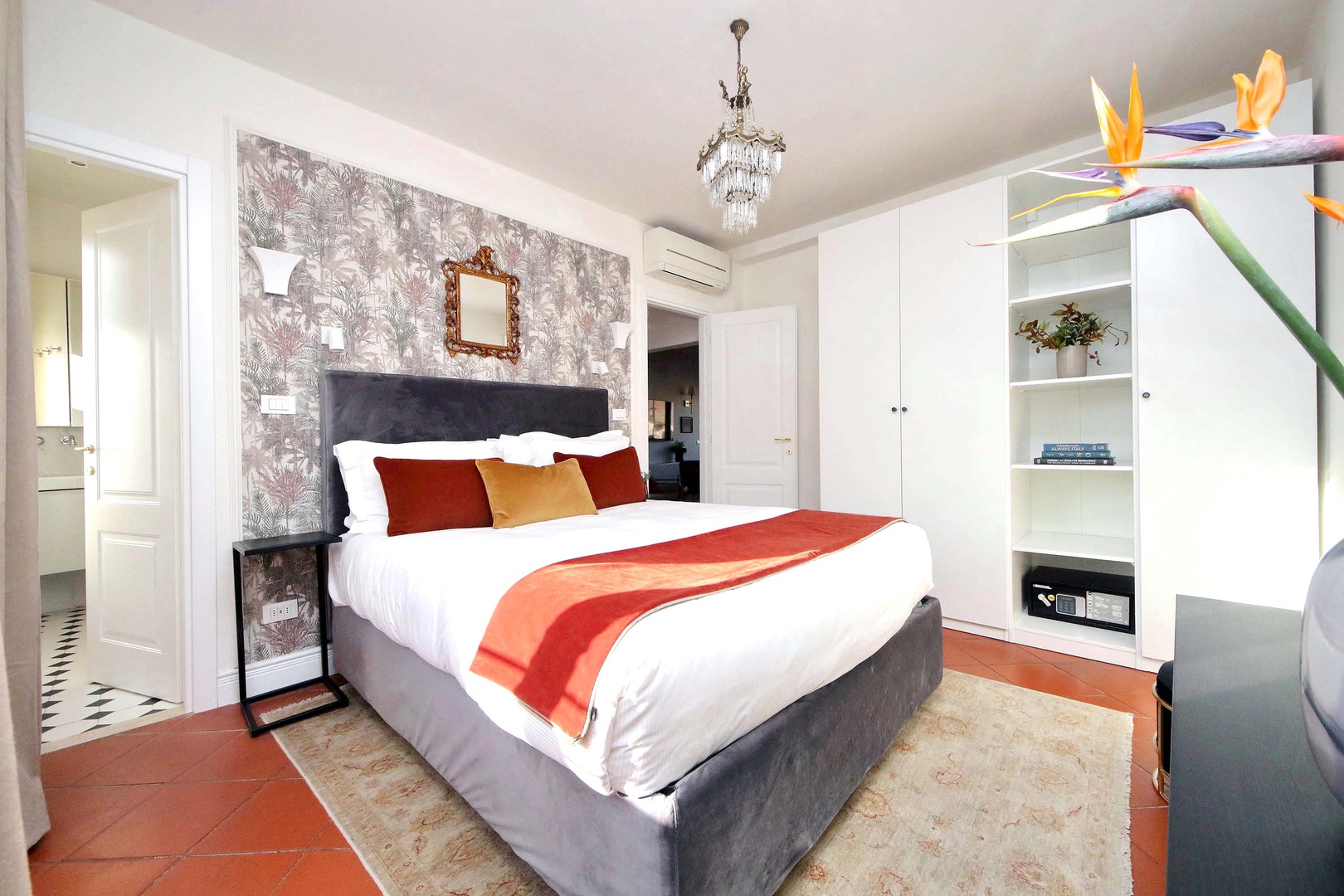 Sink into your plush bed with crisp linens and colorful throw pillows. The elegant chandelier and tropical blooms create a serene retreat.