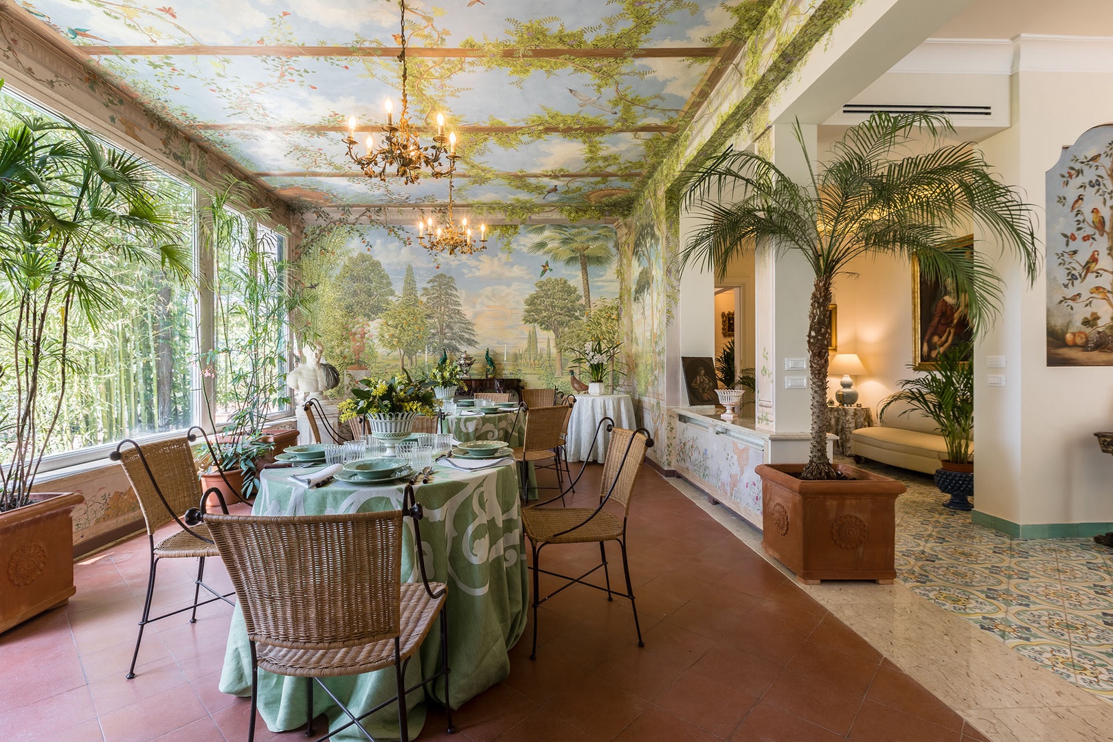 Large dining room brings the outdoors inside with lush greenery and tromp l'oeil imagery.