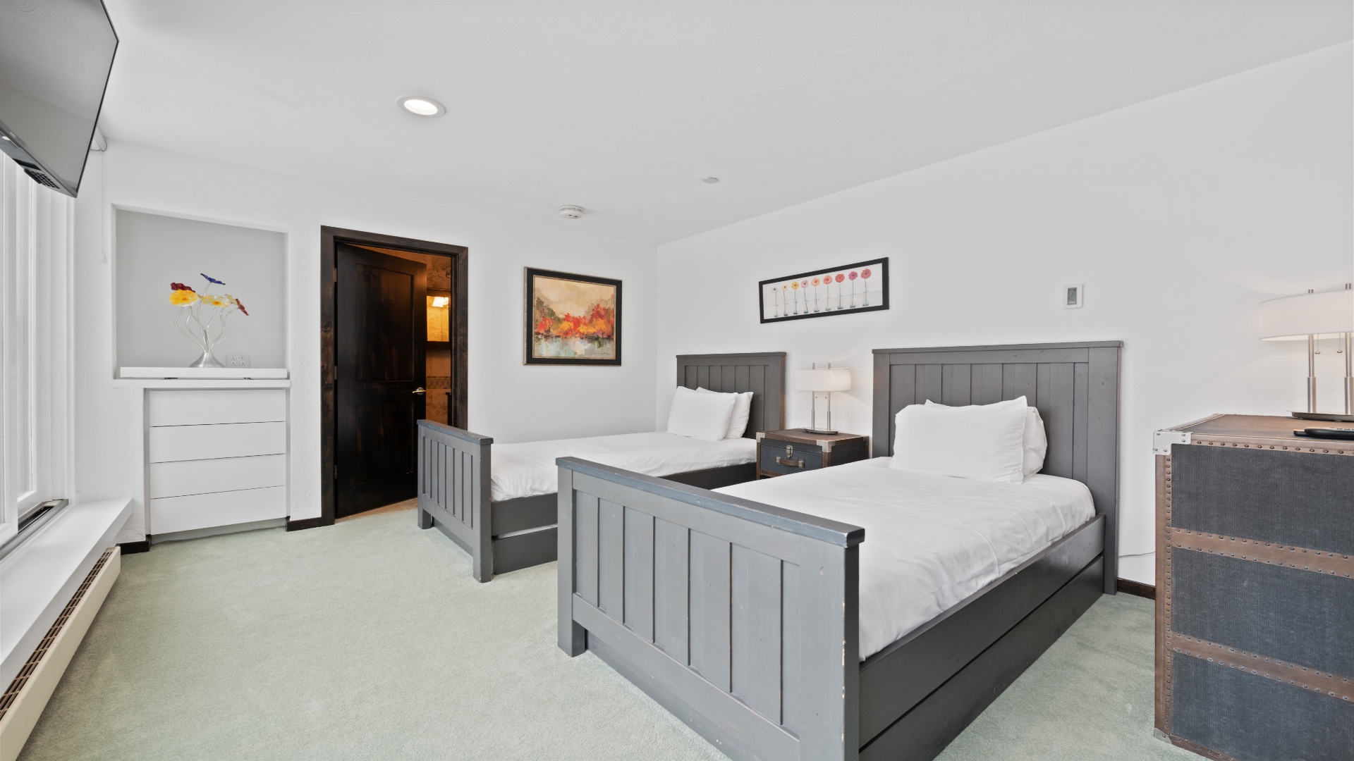 Your restful bedroom retreat features two cozy beds with crisp linens, warm wood accents, modern artwork, and your own TV for lazy mornings in.