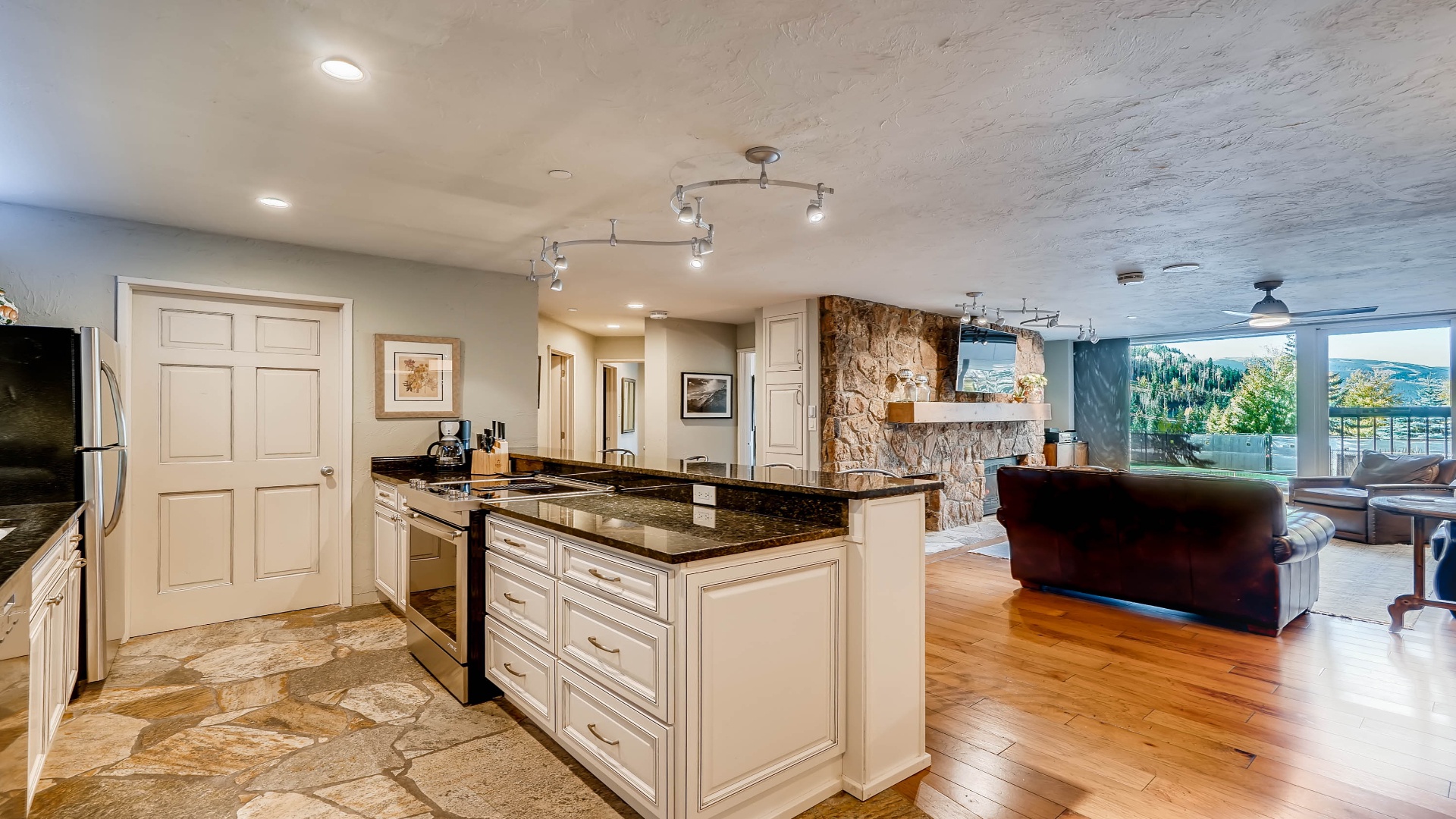 Your open-concept space flows effortlessly from kitchen to living area, where mountain views greet you through floor-to-ceiling windows and warm wood floors invite you to unwind.