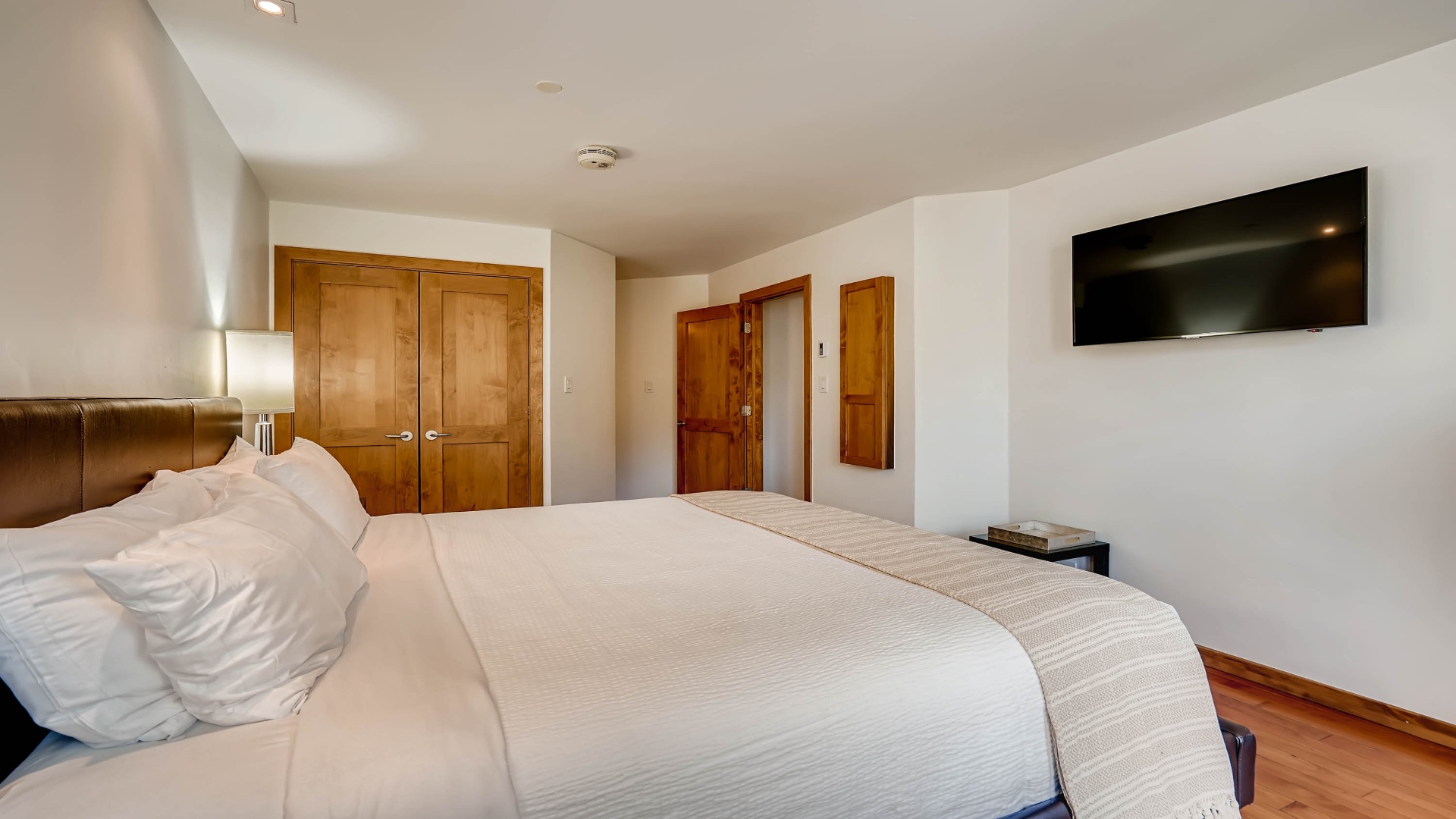 Sink into crisp white linens on your plush bed, where modern comfort meets warm wood accents. Wake to natural light, unwind with your favorite shows, and store all your belongings with ease.