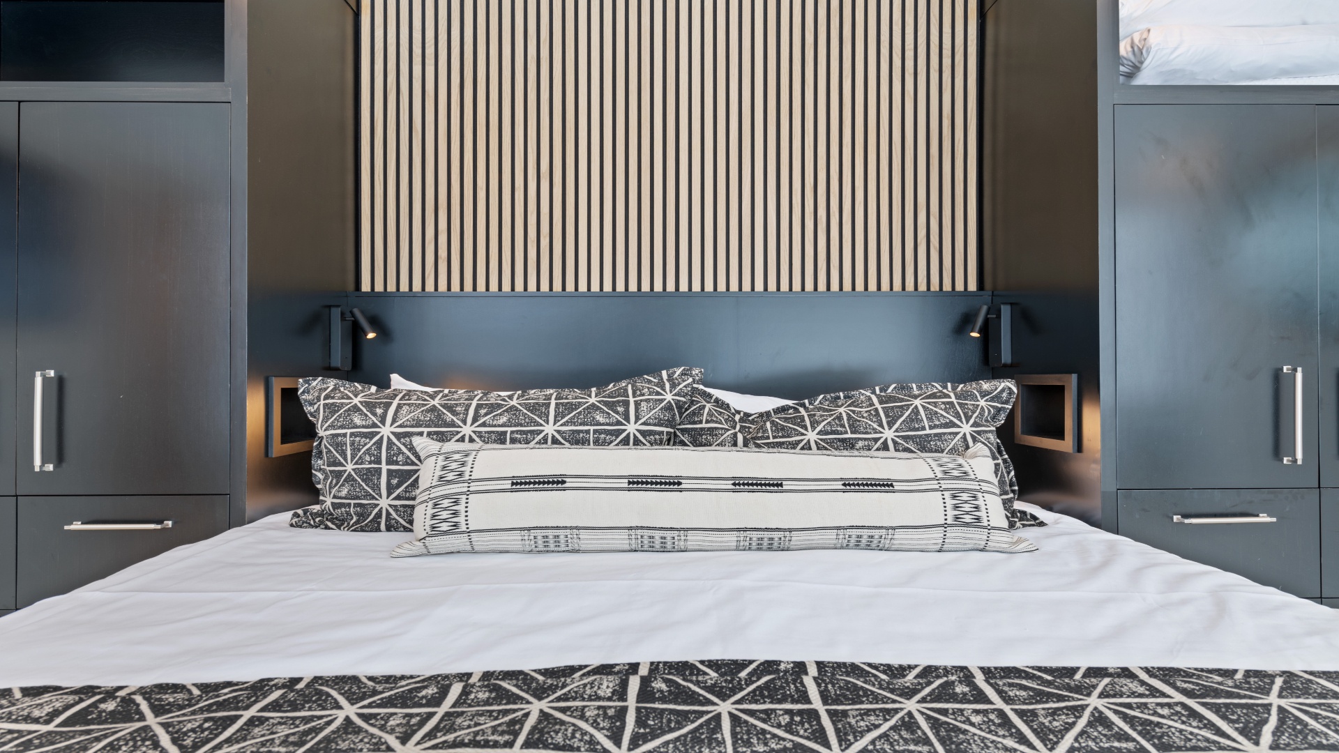 Sink into crisp linens and modern style. Your bedroom features a statement wood-slat headboard, sleek reading lights, and ample storage—perfect for unwinding after exploring.