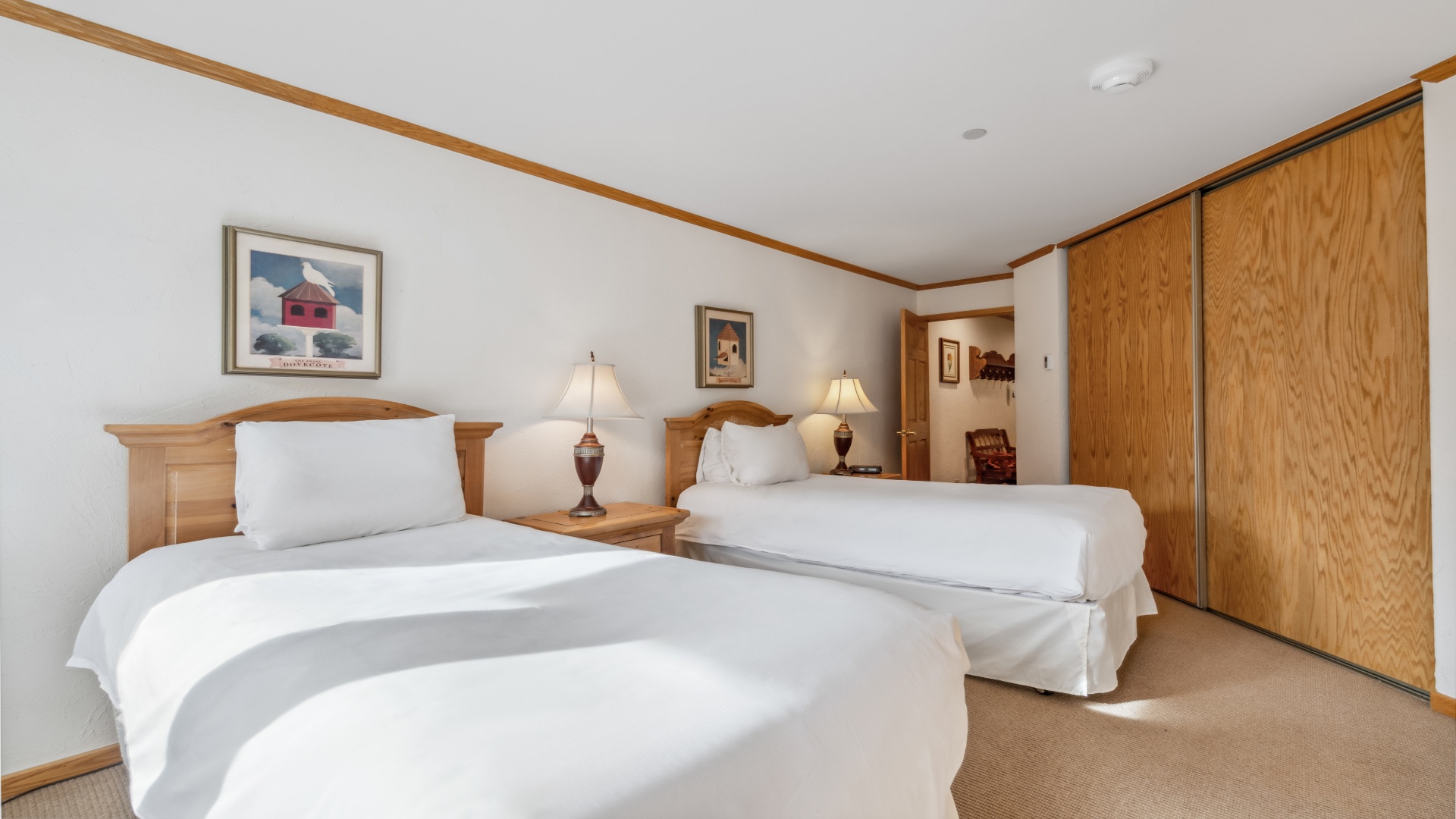 Unwind in your comfortable bedroom with two plush beds, warm wood accents, soft lighting, and ample closet space for your belongings—a restful retreat awaits you.