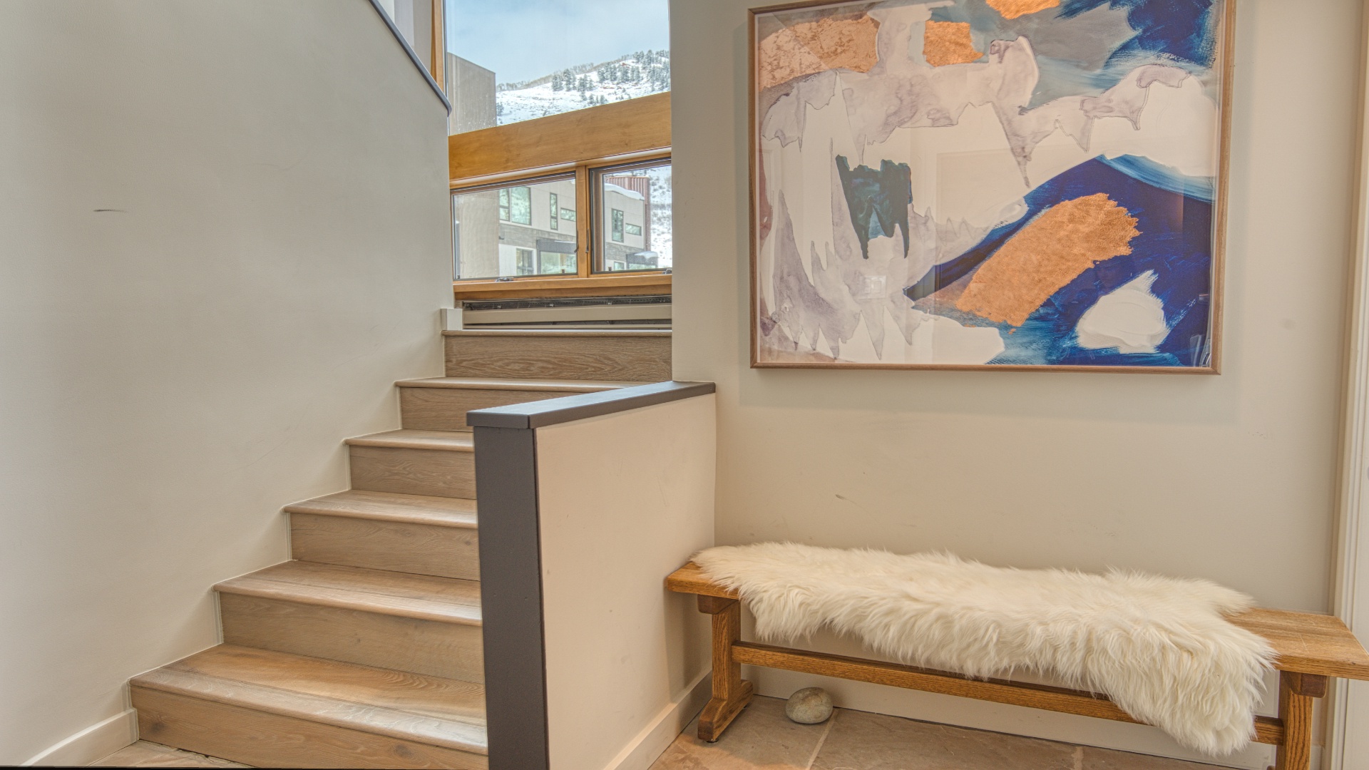A cozy nook with a plush bench invites you to pause, while natural light pours in from mountain-view windows above the warm wooden staircase—your gateway to the rest of the home.