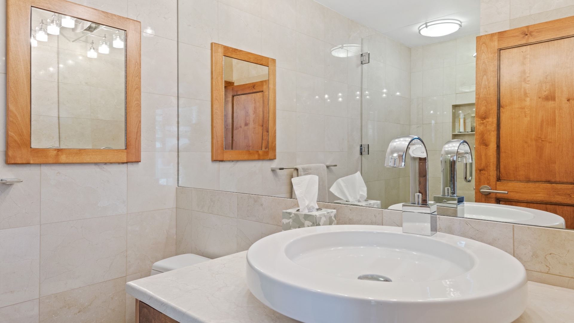 A bright, modern bathroom awaits, featuring a sleek vessel sink, walk-in glass shower, and warm wood accents that create a spa-like retreat for your stay.