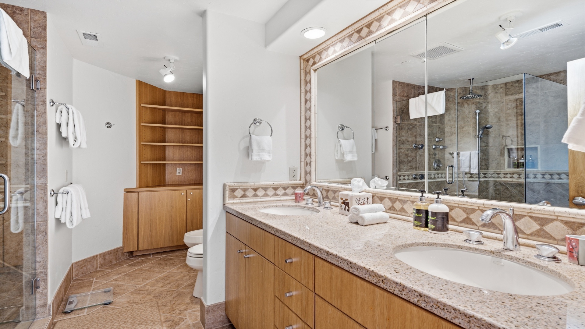 Step into your luxurious bathroom with warm wood cabinetry, dual vanities, and a spacious glass-enclosed shower. Fresh towels await your arrival.