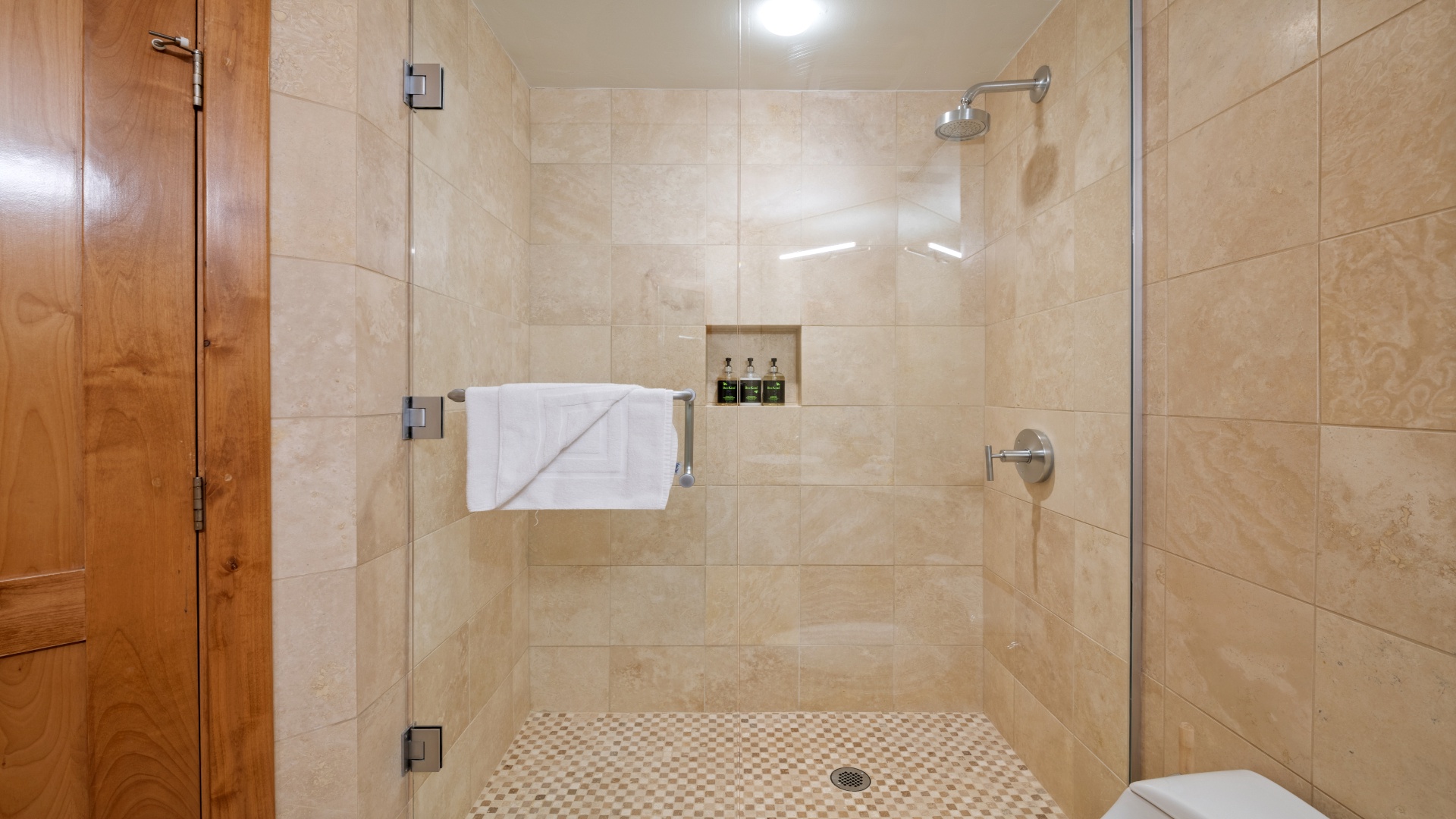 Step into your private spa-like shower with elegant travertine tile, rainfall showerhead, and fresh towels ready for your ultimate relaxation.