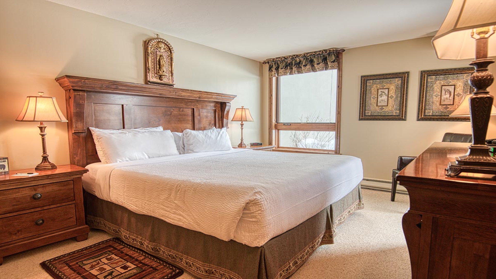Sink into crisp linens and soft pillows in your cozy bedroom retreat. Natural light streams through the window, illuminating elegant wood furnishings and thoughtful décor for your perfect mountain escape.