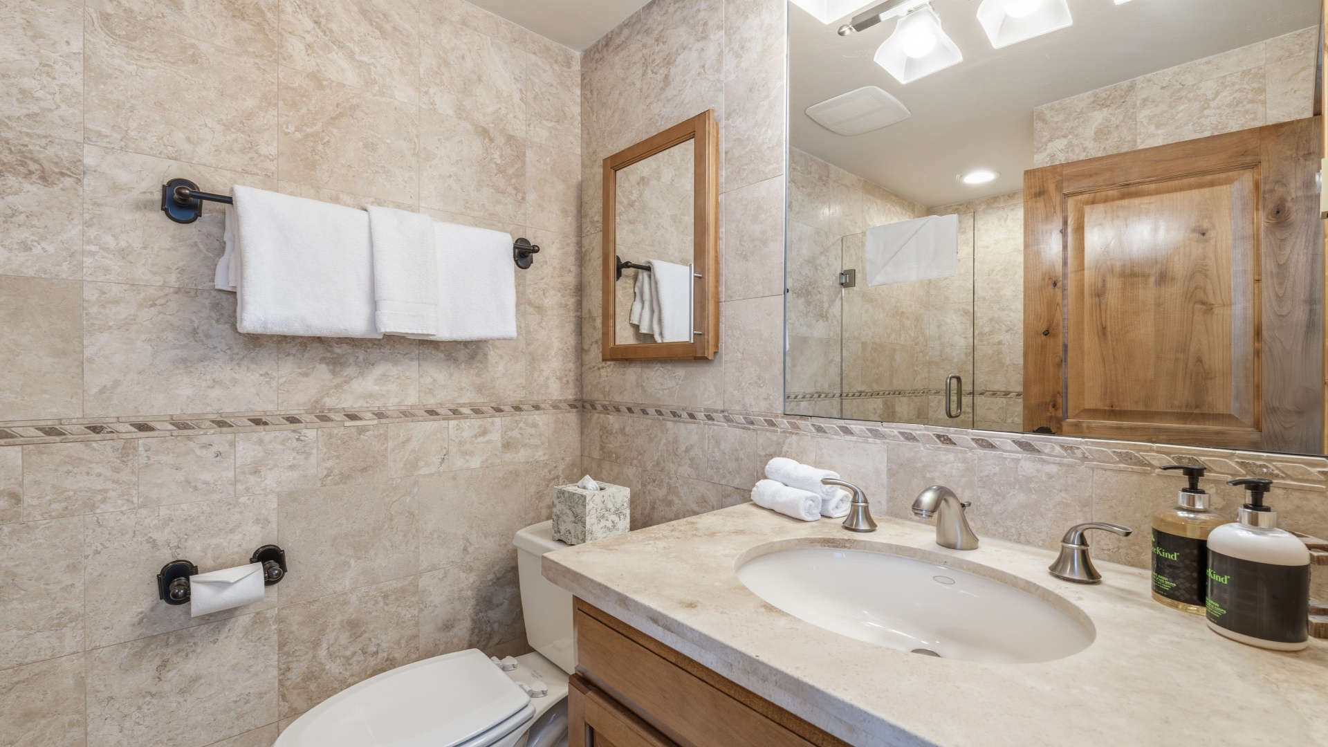 Your private bathroom features elegant marble-style tiling, a spacious vanity, and a sleek glass-enclosed shower. Fresh towels and premium amenities await your arrival.
