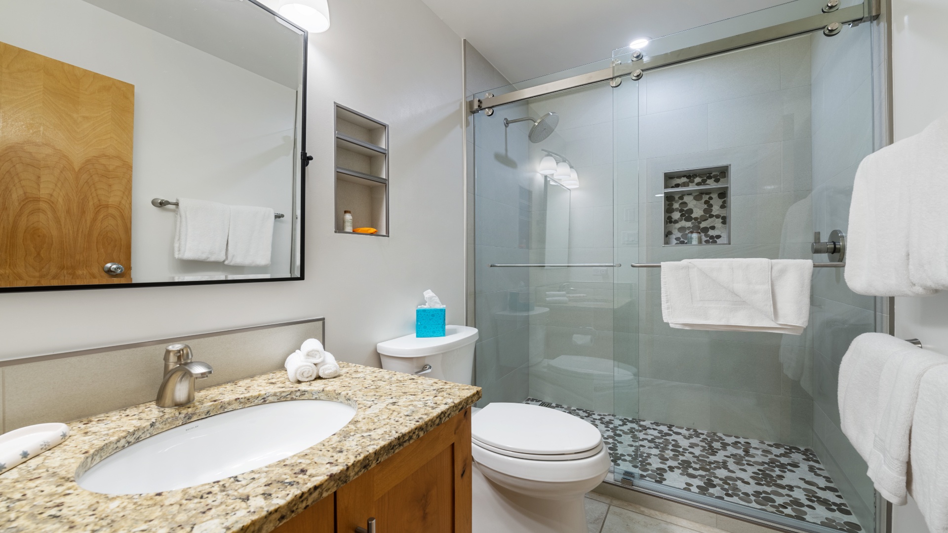 Step into your private bathroom featuring a sleek walk-in shower, granite vanity, and fresh towels awaiting your arrival. The pebble tile floor and modern fixtures create a spa-like retreat for your stay.