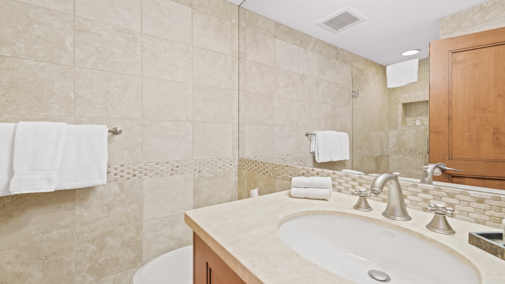 Step into this spa-like bathroom where elegant travertine tiles and a soothing neutral palette create your private sanctuary. Fresh towels await you after a refreshing shower.