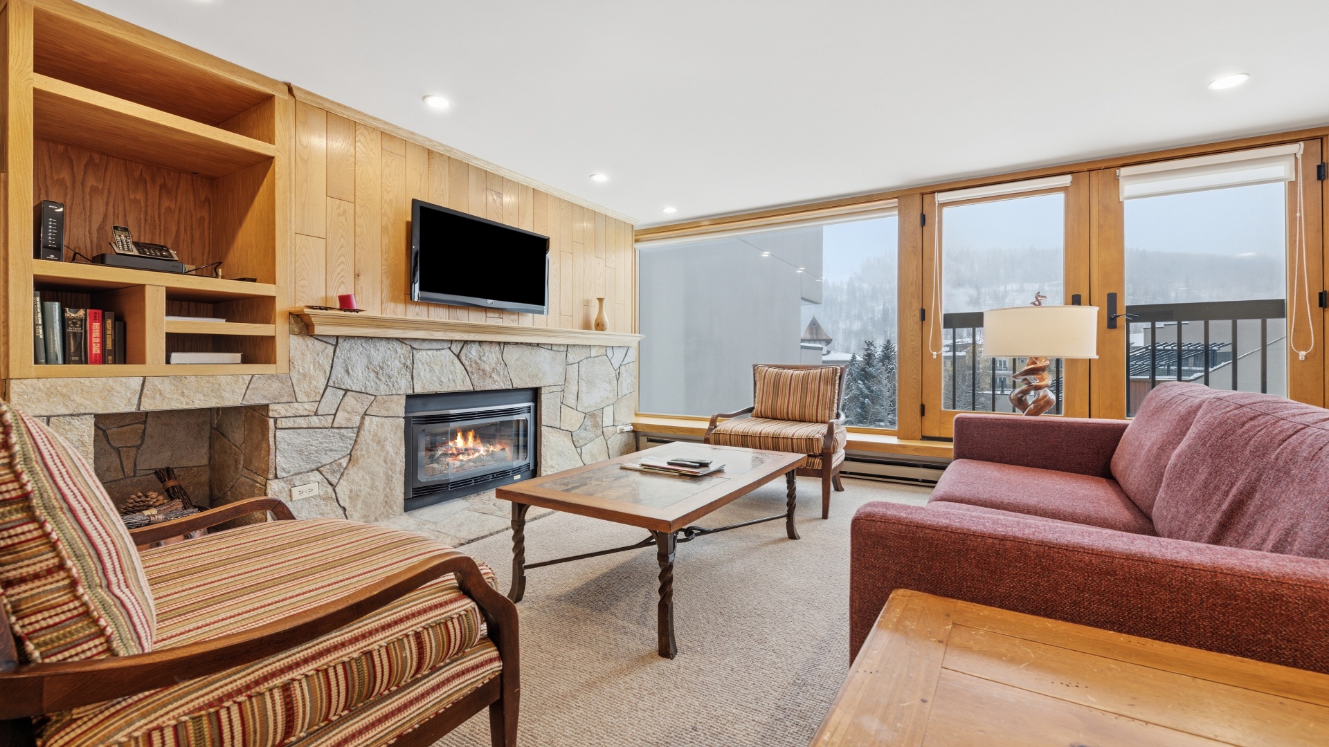 Cozy up by your stone fireplace while gazing at snowy mountain views through floor-to-ceiling windows. Warm wood tones and comfortable seating create the perfect alpine retreat after a day on the slopes.