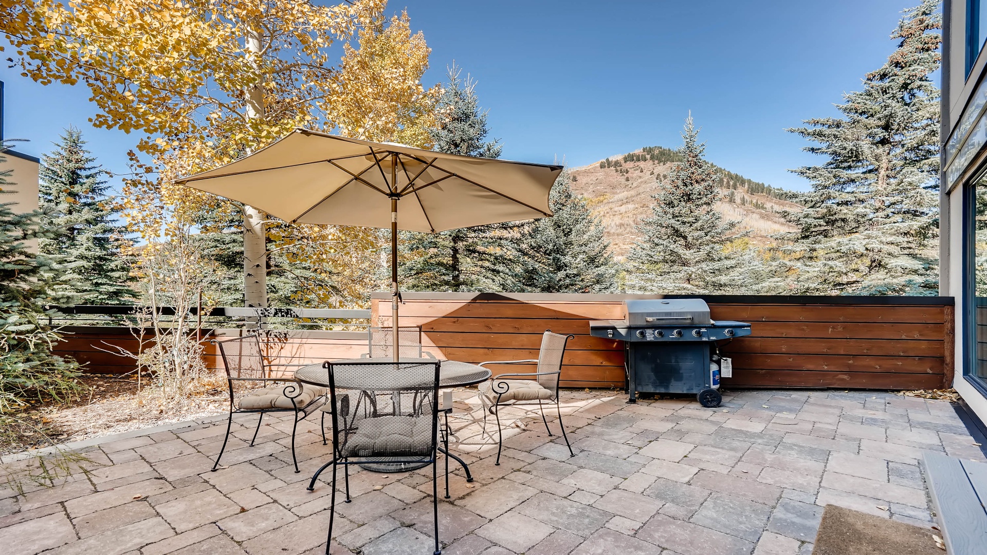 This property sits at the base of a mountain, surrounded by golden autumn foliage and evergreens. Paved patio features outdoor dining and barbecue area with scenic mountain views.