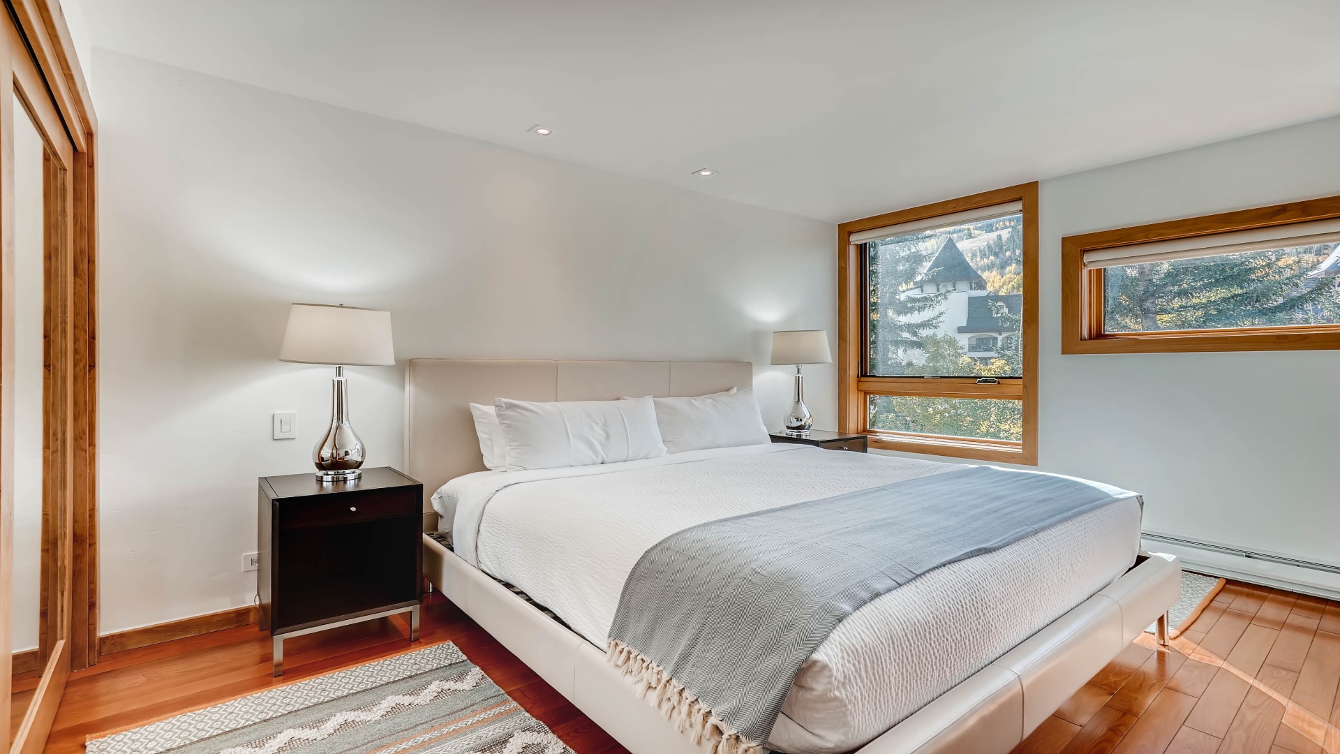 Unwind in your serene bedroom with plush linens, warm wood accents, and peaceful mountain views framed by generous windows that fill the space with natural light.