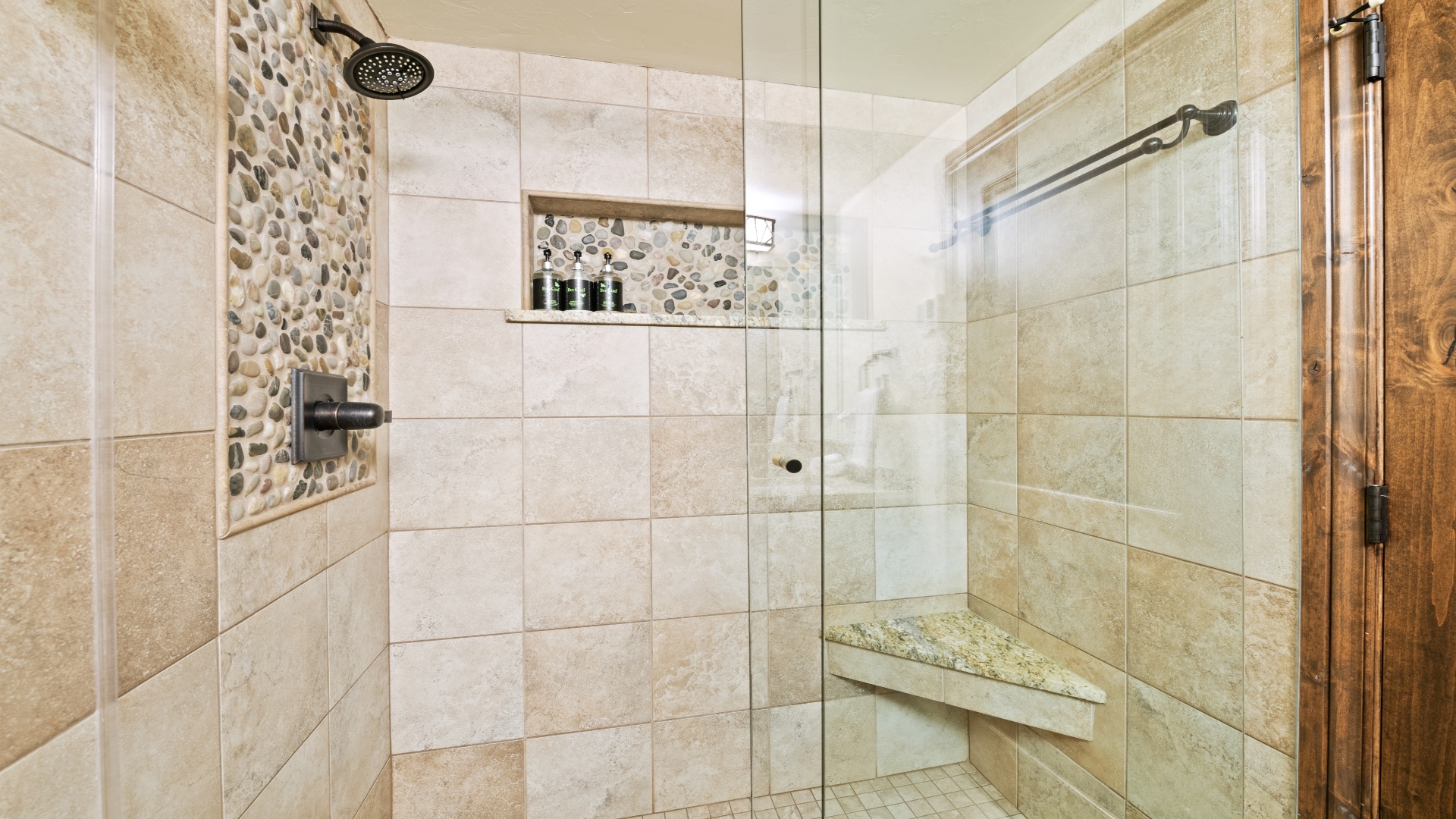 Step into a beautifully tiled walk-in shower with elegant pebble accent walls, rainfall showerhead, built-in bench, and niche storage—your private oasis awaits.