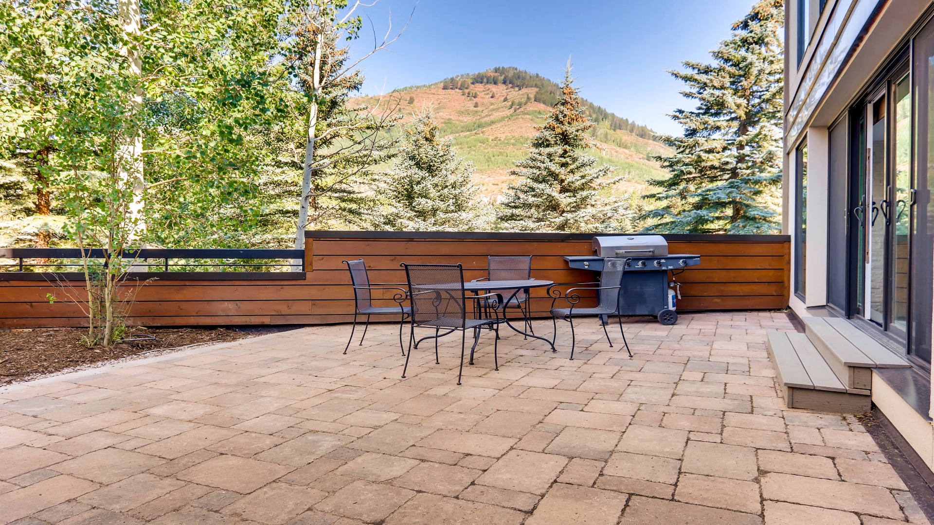 Your private patio invites outdoor dining with mountain views, a BBQ ready for grilling, and a peaceful backdrop of evergreens and rolling hills.