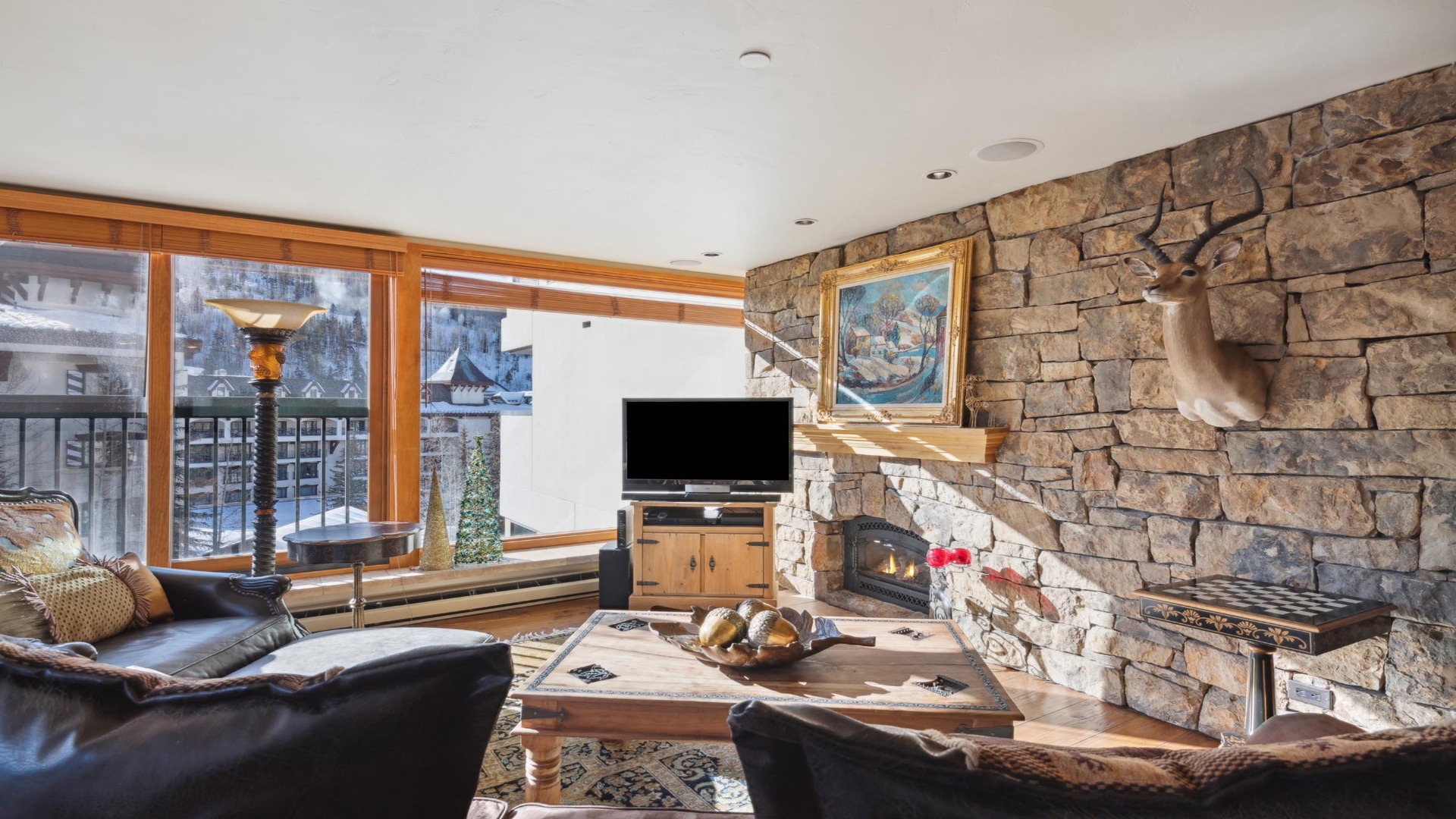 Sink into plush leather seating by your stone fireplace, where mountain views frame cozy evenings and natural textures create warmth throughout your alpine retreat.