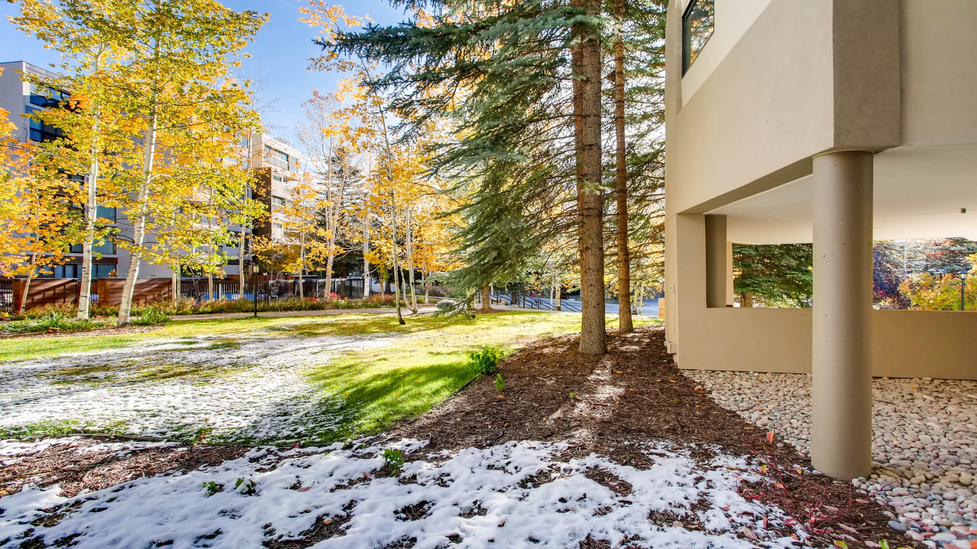 Modern property entrance surrounded by vibrant autumn foliage and tree-lined grounds with patches of early snow creating a serene seasonal setting.