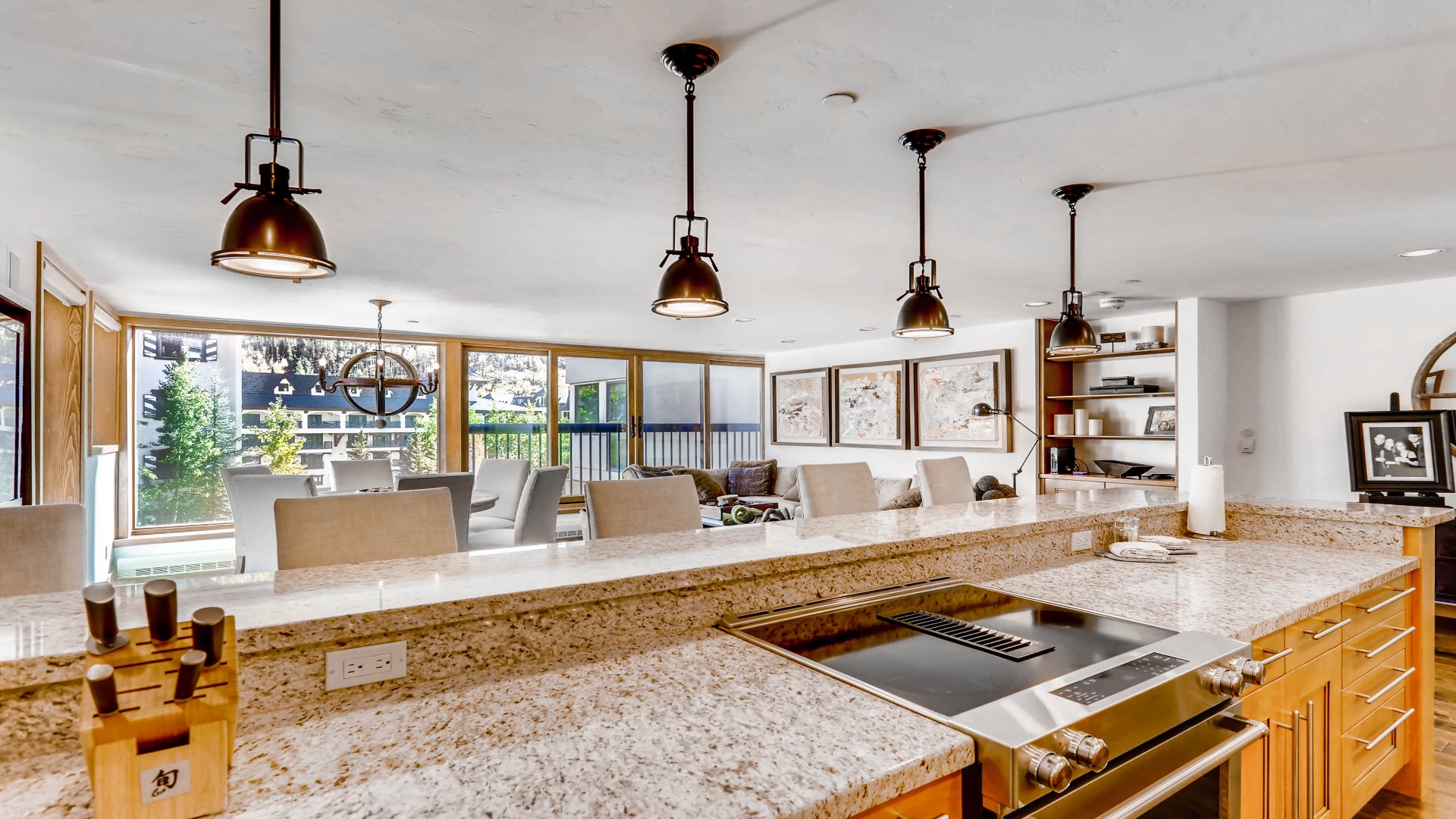 Step into your gourmet kitchen where granite countertops gleam under industrial pendant lights. Cook and entertain with ease as natural light floods through expansive windows, framing your cozy living space beyond.
