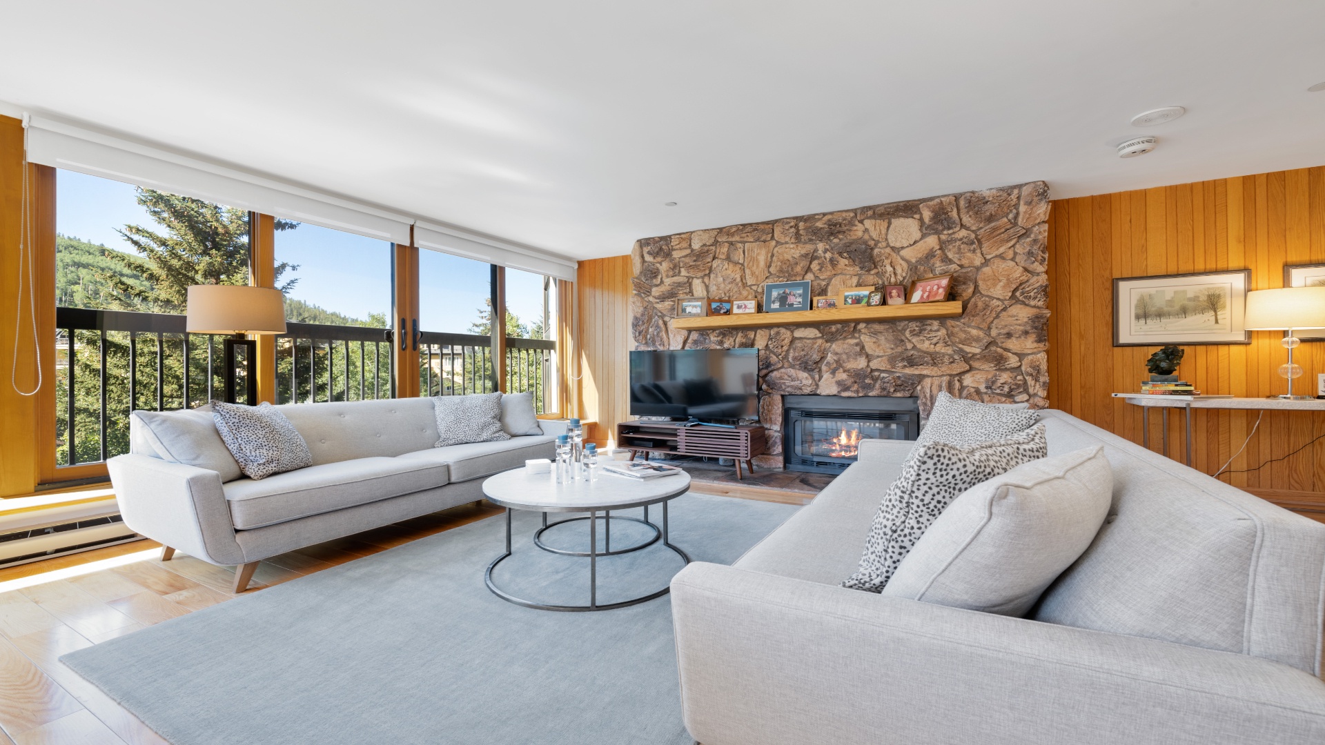 Unwind in your spacious living room with a cozy stone fireplace, modern furnishings, and floor-to-ceiling windows framing serene forest views—your perfect retreat.