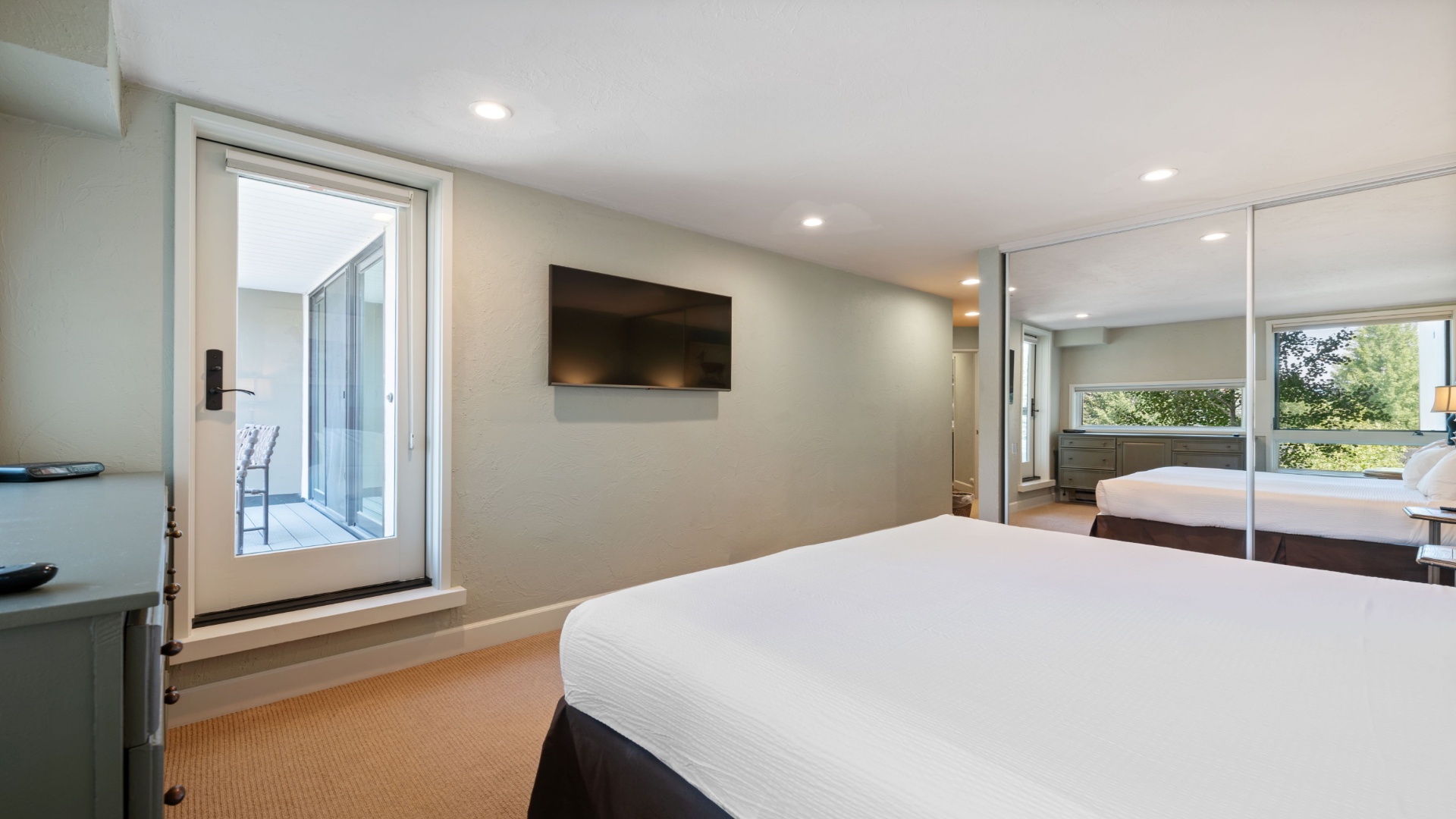 Your sleek, modern bedroom awaits with crisp linens, a wall-mounted TV, and serene views of greenery—designed for restful nights and peaceful mornings.