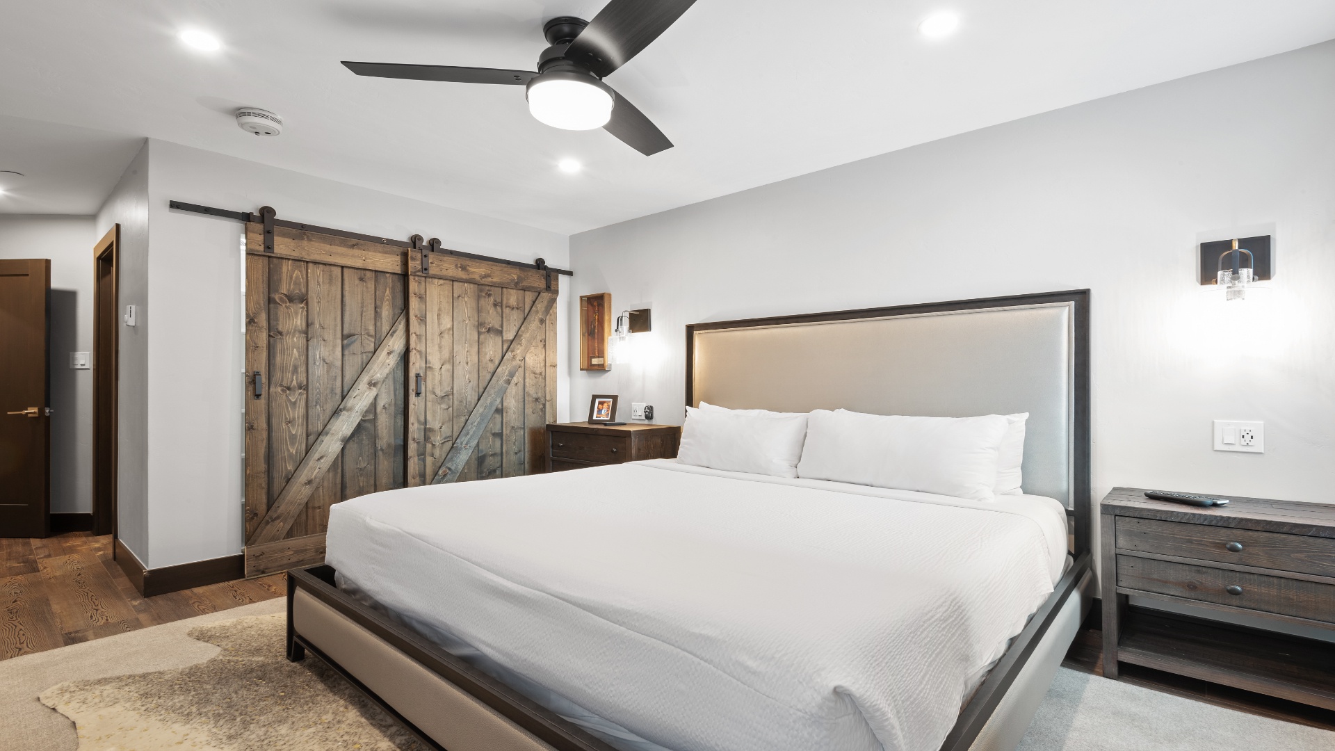 Your spacious bedroom features a plush bed with crisp linens, rustic barn doors, and a modern ceiling fan—a perfect blend of comfort and style for your restful retreat.