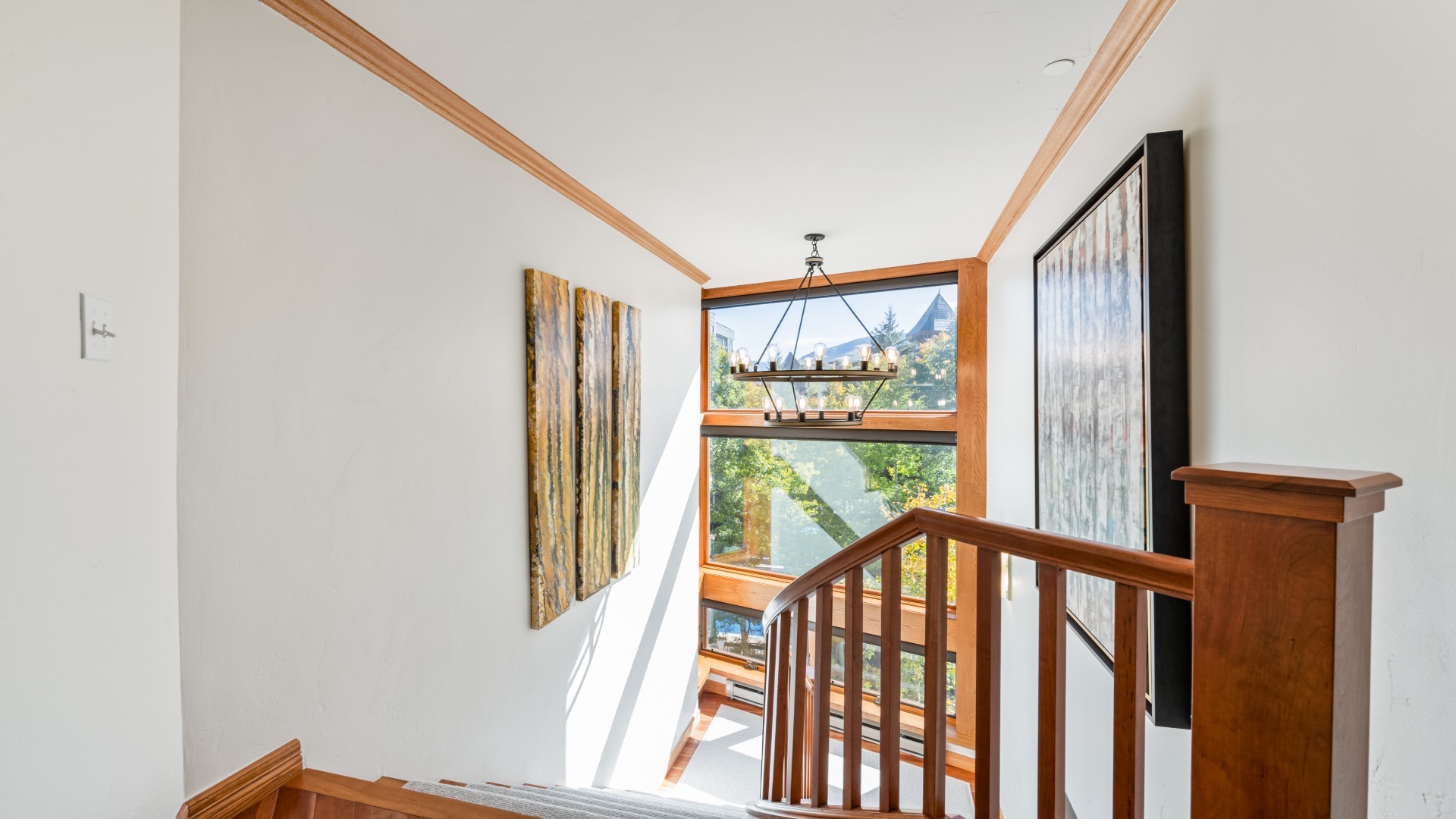 Sunlight streams through expansive windows, framing stunning mountain and forest views from this bright stairwell landing. Your vacation begins as you climb these warm wood stairs.