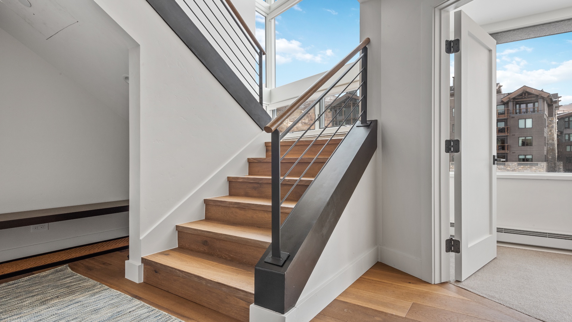 A modern staircase with warm wood steps and sleek metal railings connects your living spaces, bathed in natural light from surrounding windows.