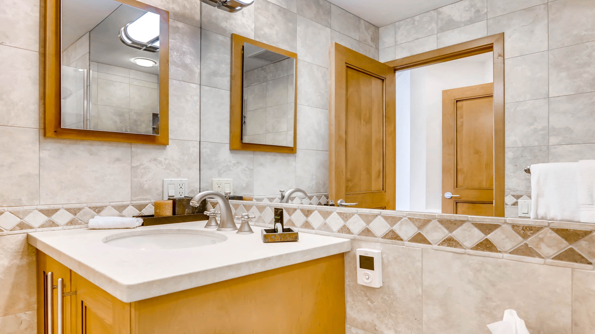 Freshen up in your private bathroom featuring elegant marble-style tiles, warm wood accents, and a spacious vanity with everything you need to feel right at home.