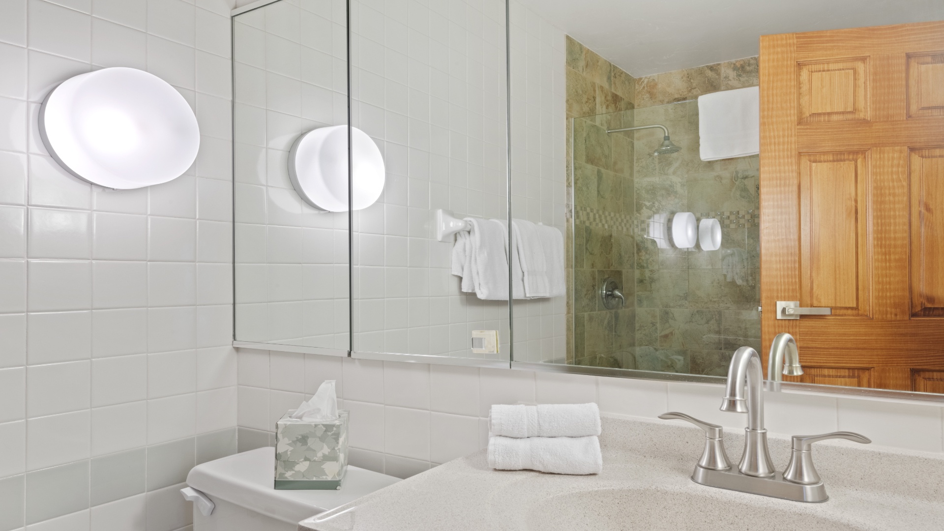 Step into your private retreat, where gleaming white tiles and warm wood tones create a spa-like sanctuary. Fresh towels await, and your rainfall shower promises a refreshing start to each day.