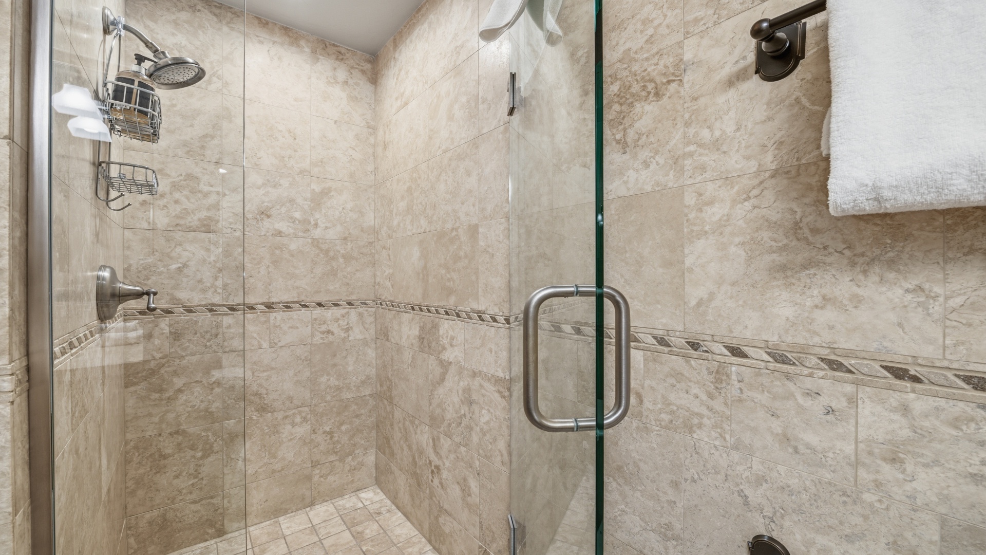 Step into your private spa-like shower with elegant travertine tile, dual rainfall and handheld showerheads, and plush towels ready for ultimate relaxation.