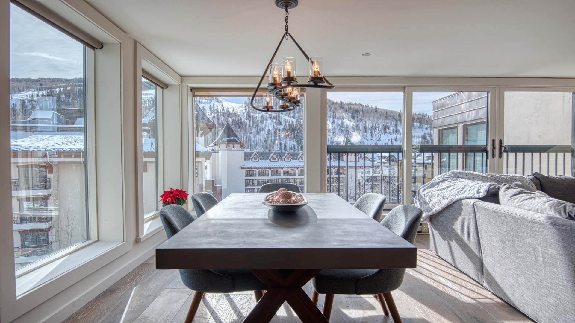 This sunlit dining area offers stunning mountain views through floor-to-ceiling windows. A stylish chandelier and sleek table create your perfect gathering spot for meals with loved ones in this alpine retreat.