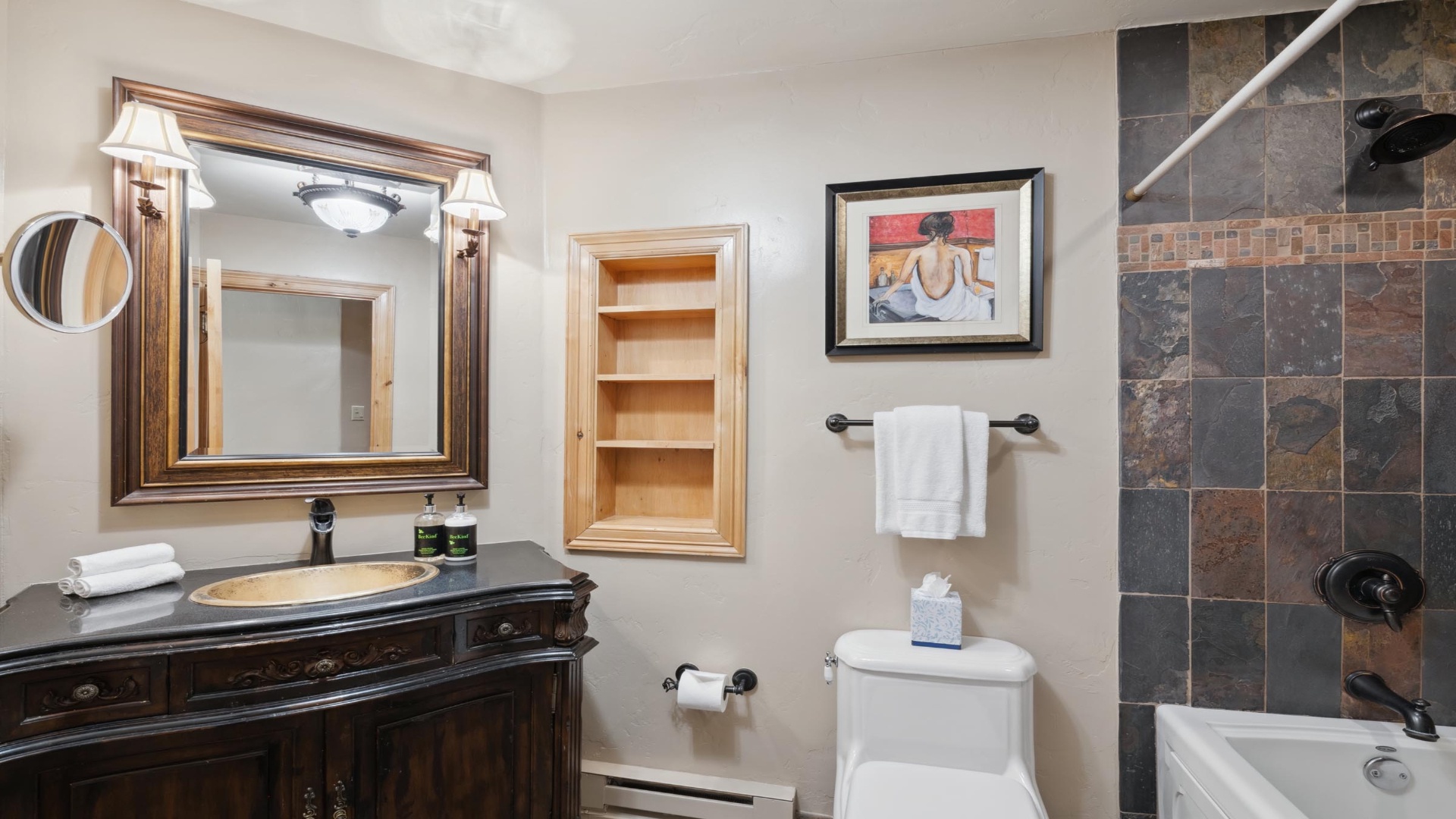 Your private bathroom blends elegant style with comfort, featuring a slate-tiled tub/shower, vanity with storage, and plush towels ready for your stay.