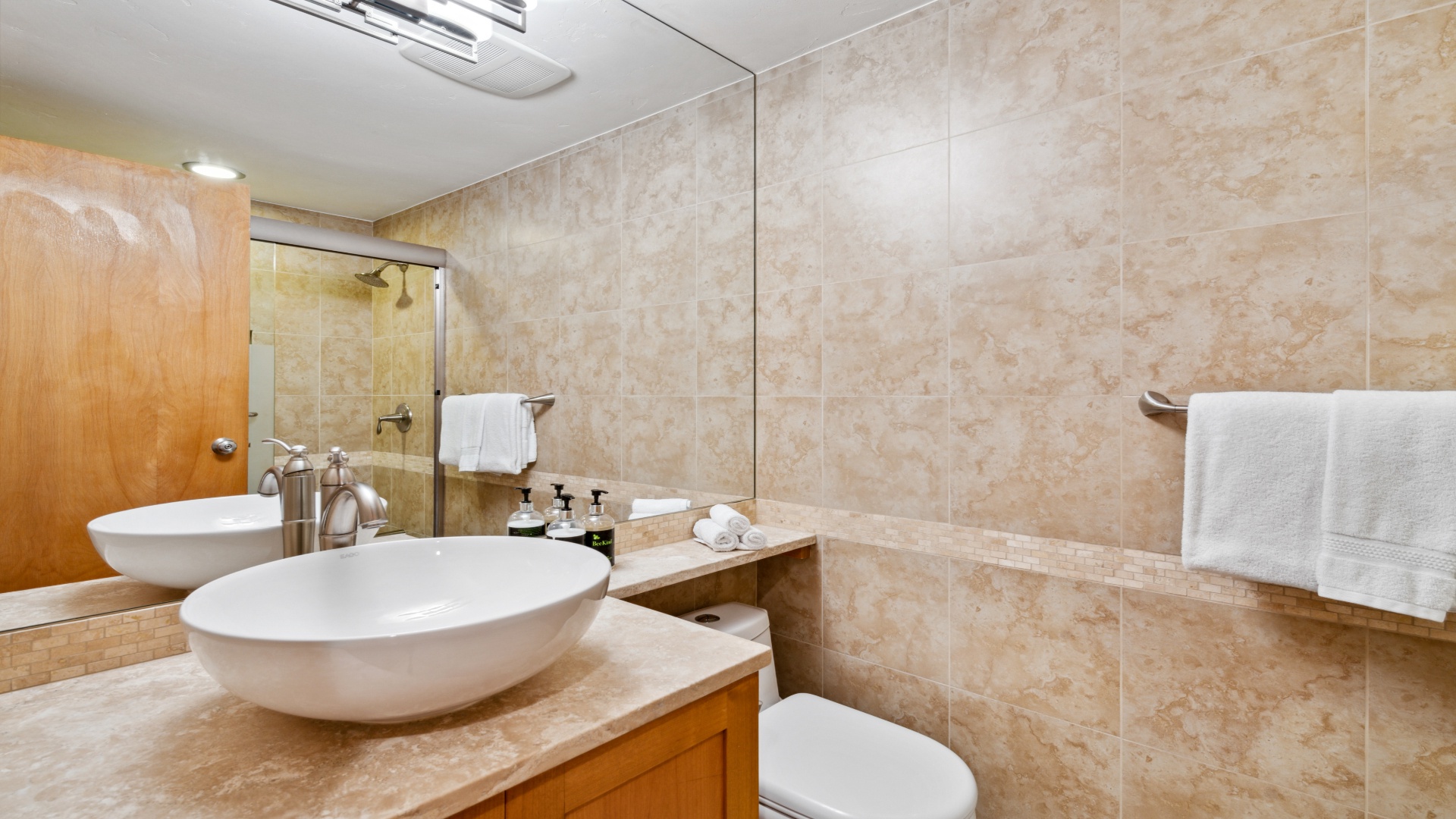 Freshen up in your elegant bathroom featuring dual vessel sinks, a spacious walk-in shower, and warm travertine tiling that creates a spa-like retreat.