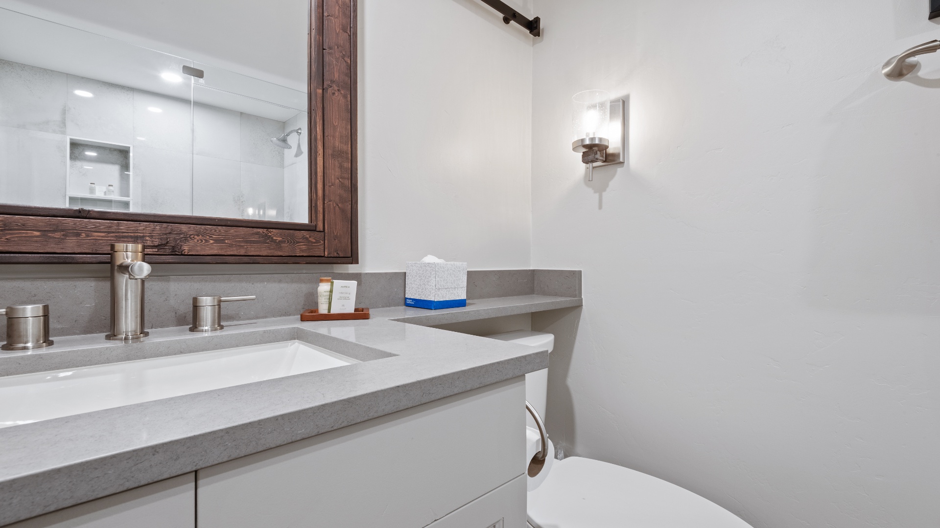 Freshen up in your modern bathroom featuring sleek gray countertops, warm wood accents, and crisp white fixtures designed for your comfort.