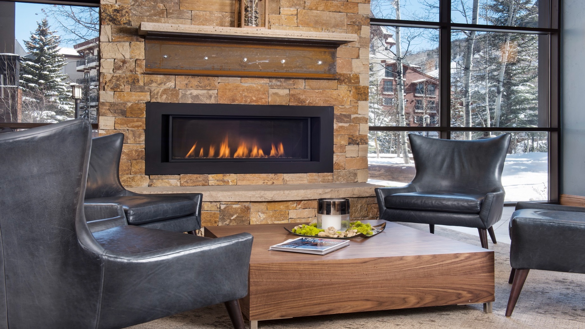 Relax in elegant leather chairs by the glowing fireplace as you take in snowy mountain views through floor-to-ceiling windows—your cozy winter retreat awaits.