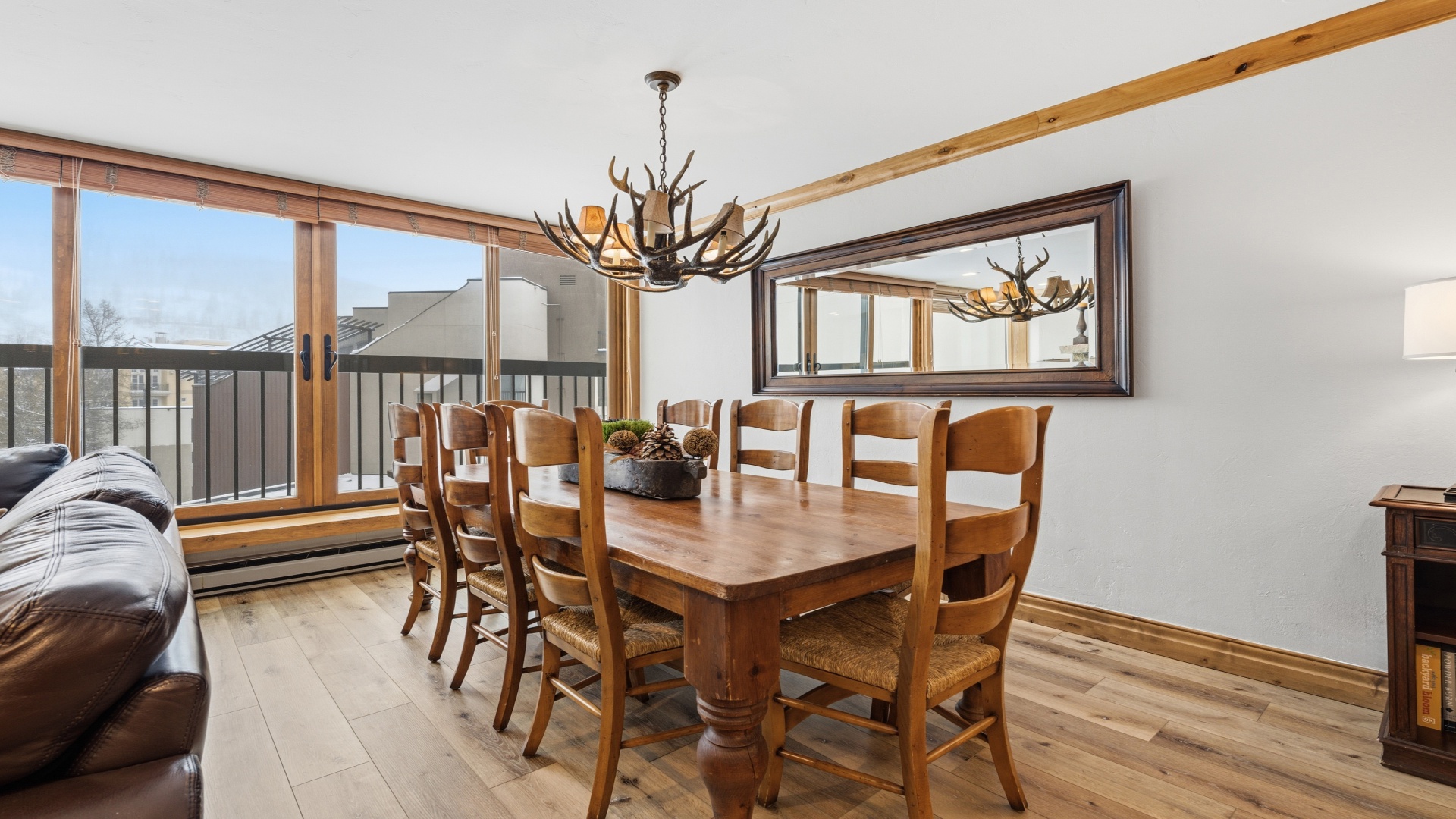 Gather around your rustic dining table for mountain-view meals beneath an antler chandelier. Large windows flood the space with natural light, creating a cozy lodge atmosphere perfect for memorable dinners together.