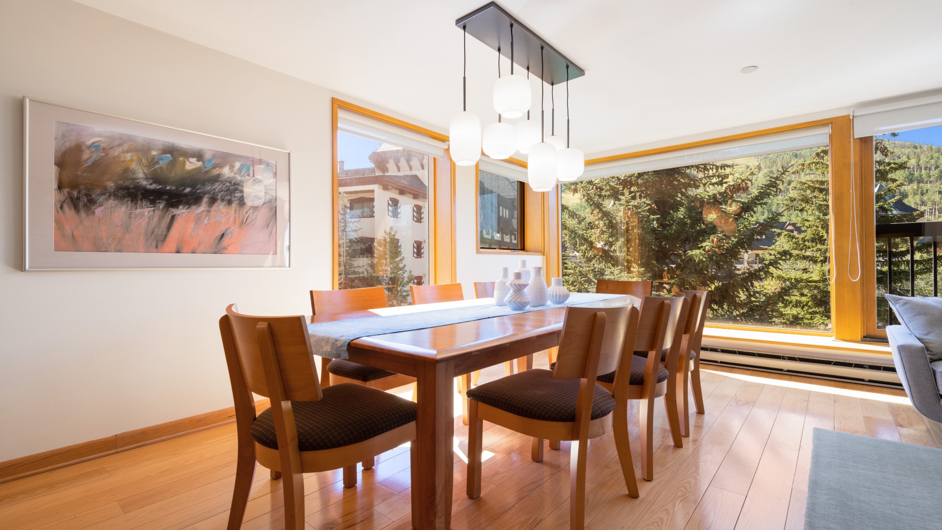 Gather around this spacious dining table bathed in natural light, where large windows frame stunning mountain views. The warm wood and modern touches create your perfect spot for memorable meals together.