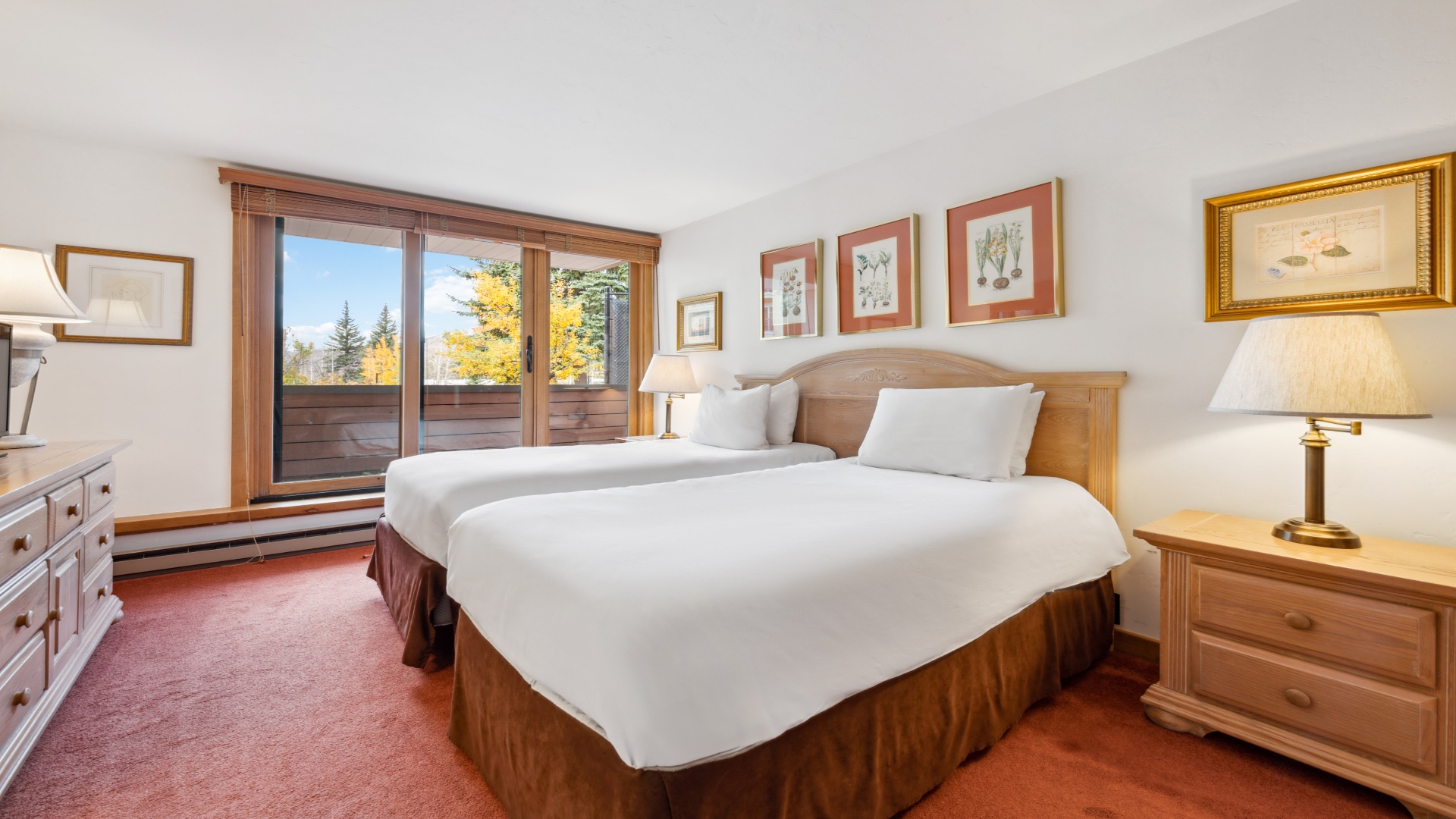 Drift off to sleep in your cozy bedroom with two plush beds, warm wood tones, and framed artwork creating a peaceful mountain retreat. Wake up to autumn views through your private balcony door.