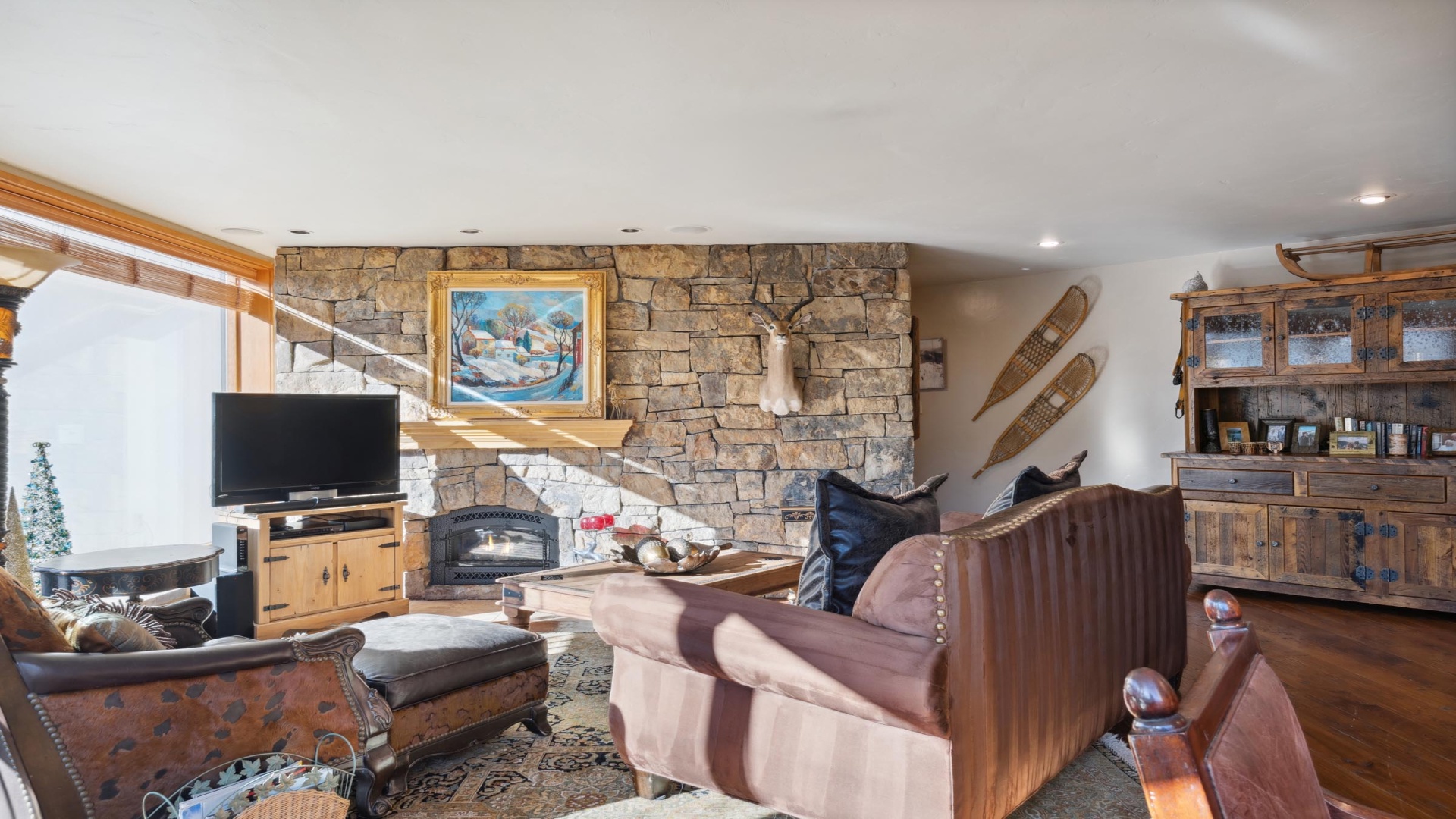 Cozy mountain retreat living room with stone fireplace, rustic wood furnishings, and vintage snowshoe decor—your perfect spot to unwind after a day on the slopes.