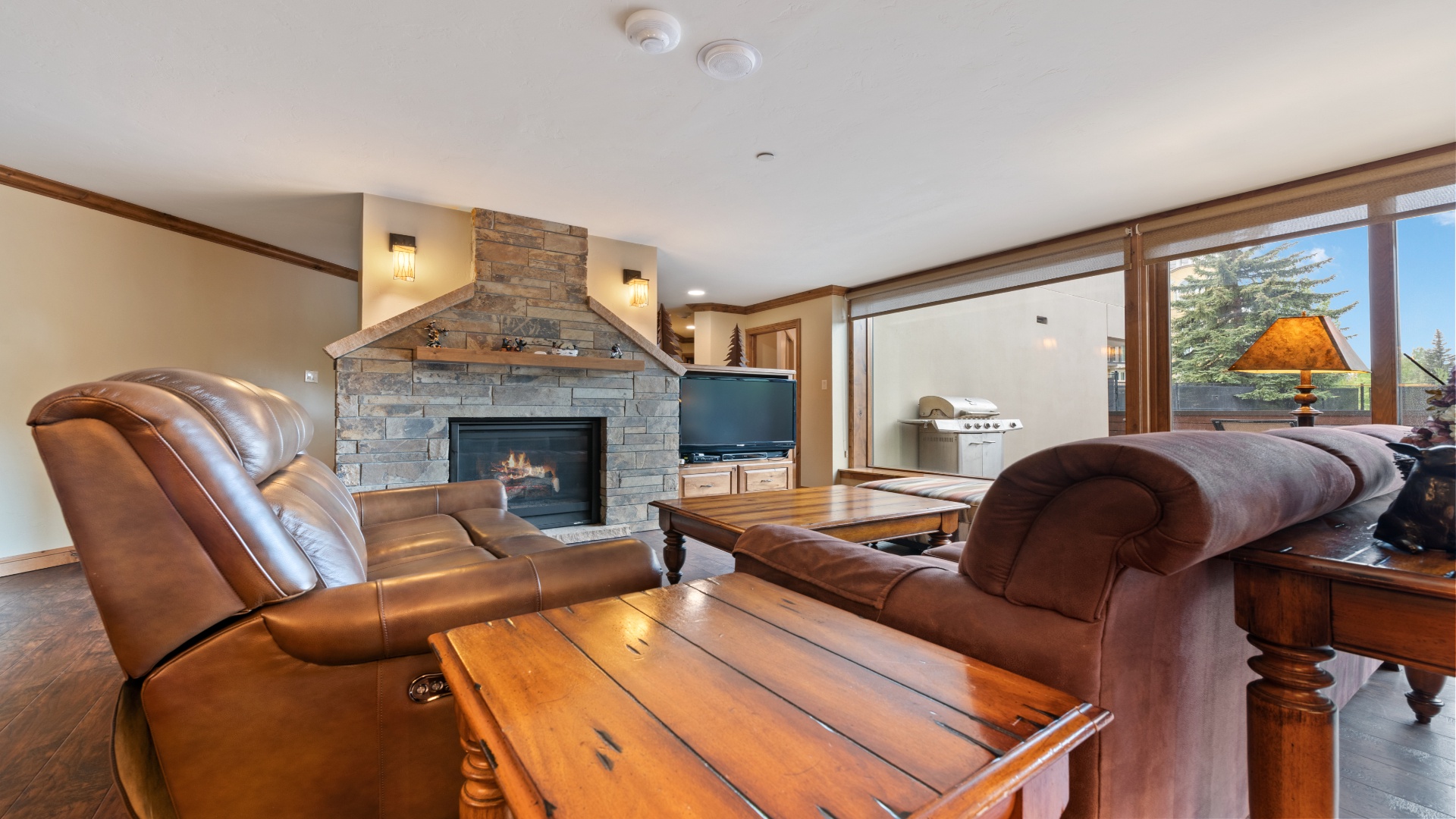 Unwind in your spacious living room where a cozy stone fireplace awaits. Sink into plush leather sofas and enjoy mountain views through floor-to-ceiling windows that frame the pines beyond.