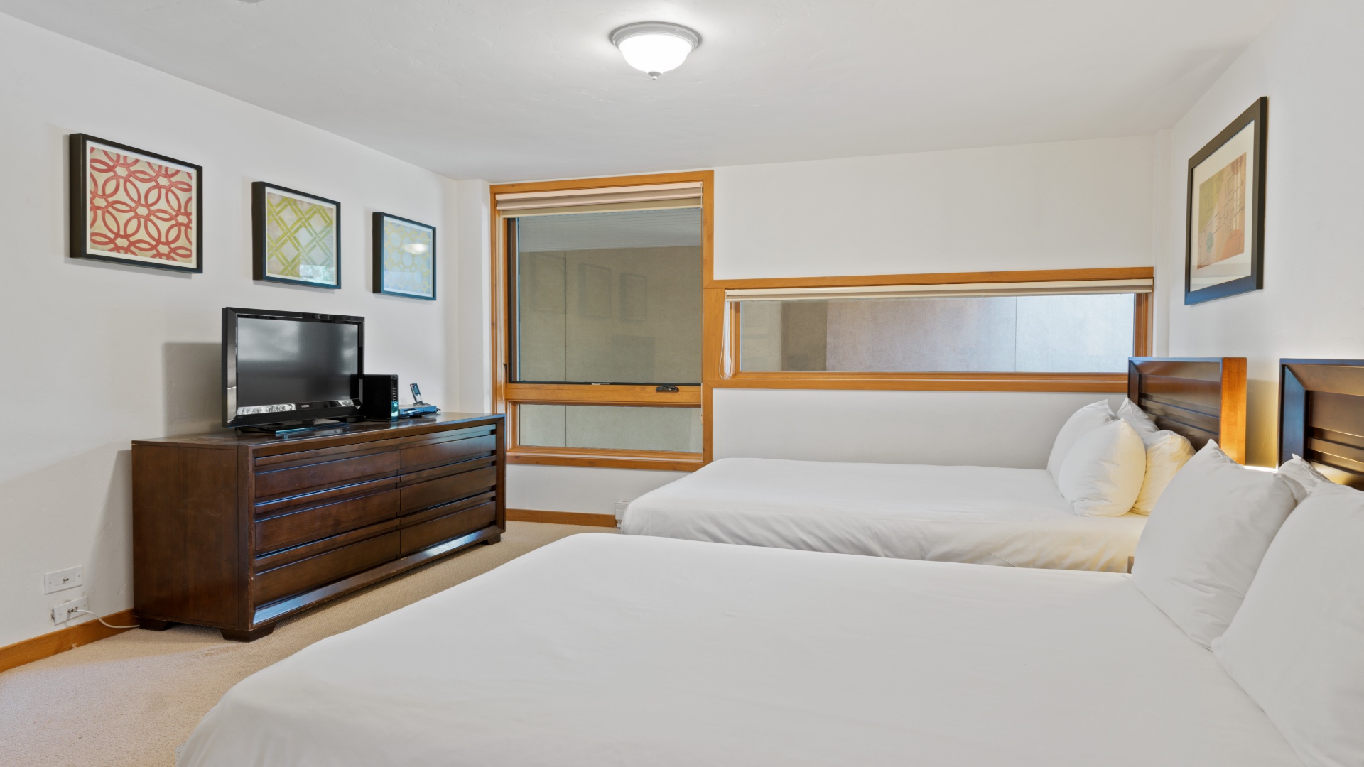 Your peaceful bedroom features two plush beds with crisp linens, warm wood furnishings, charming framed art, and a TV for your entertainment and relaxation.