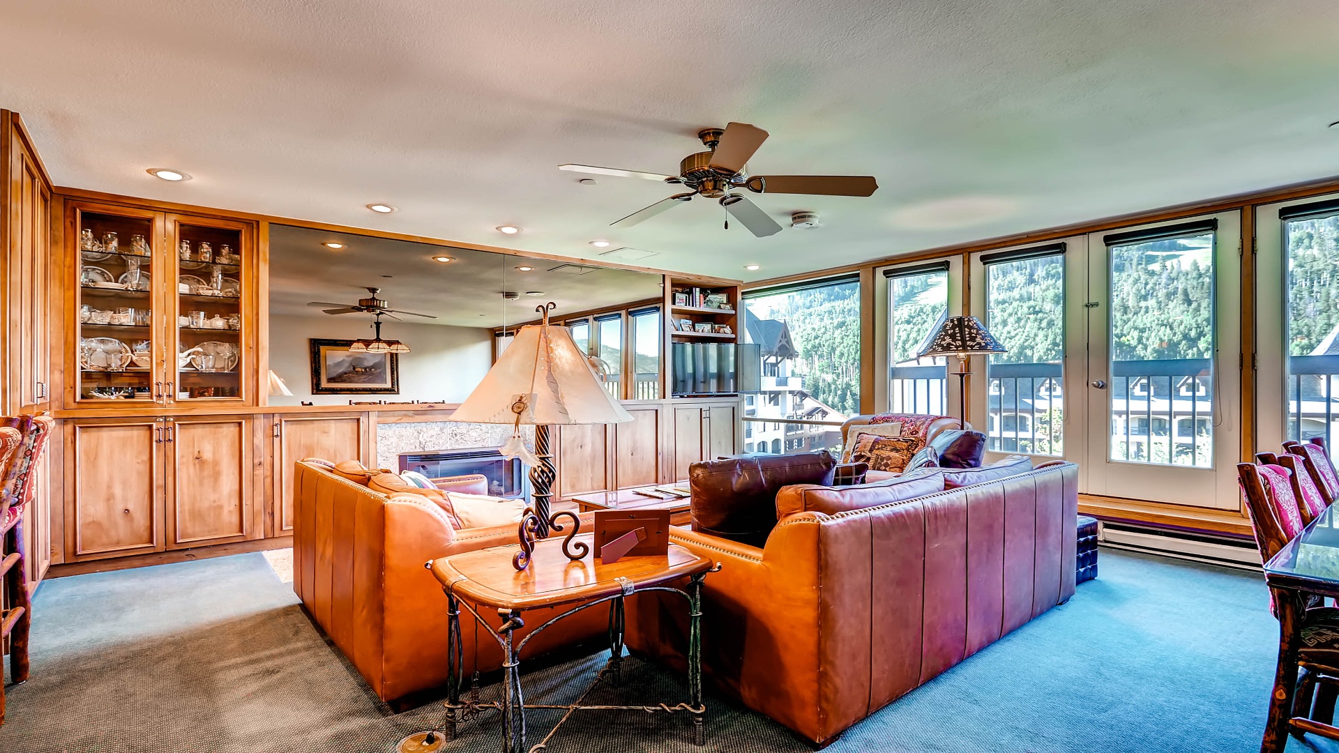 Relax in your spacious living room with plush leather sofas, warm wood accents, and expansive windows framing stunning mountain vistas—your perfect retreat awaits.